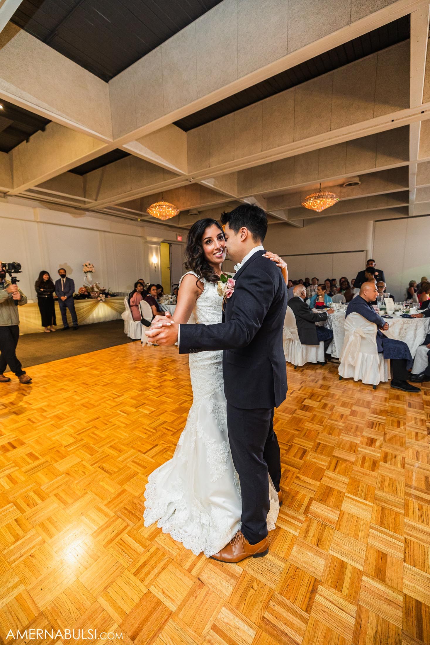 Newlyweds share their first dance on a wooden parquet floor during their wedding reception.