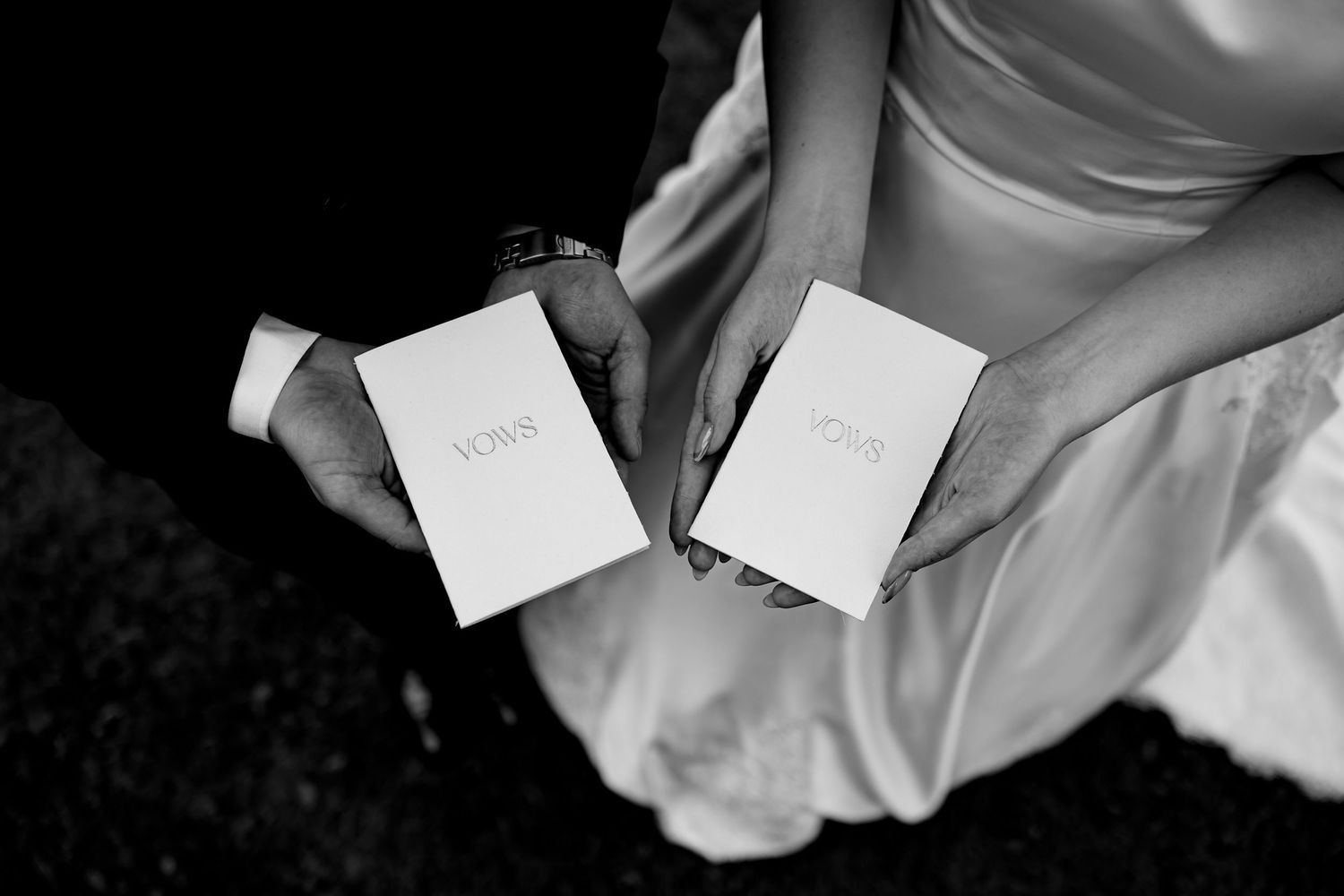 Bride and groom hold matching white vow booklets together during wedding ceremony in black and white.