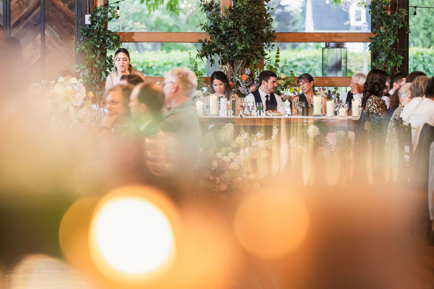 Guests seated at long wedding reception table adorned with lush greenery and floral arrangements.
