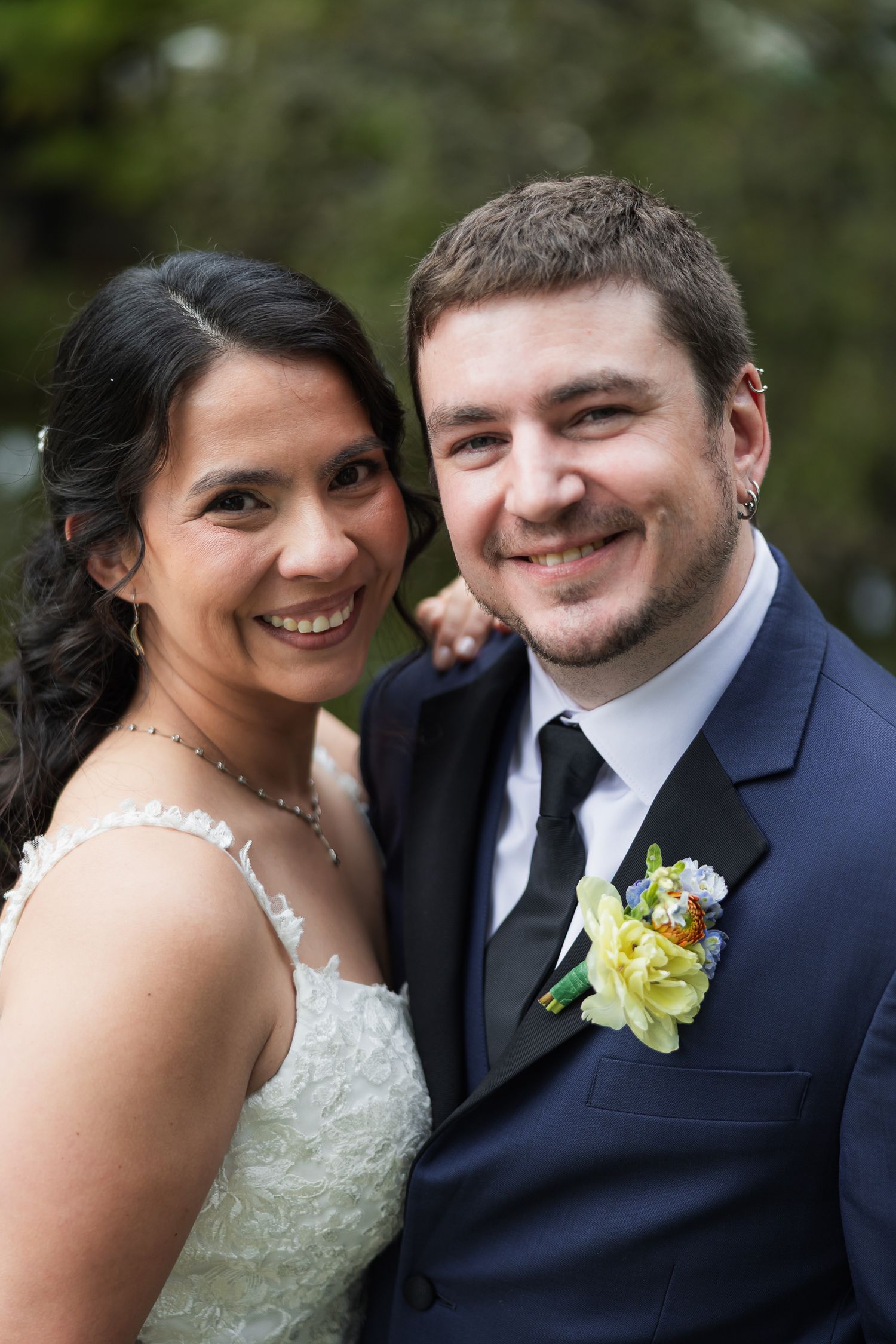 Smiling bride and groom pose together on their wedding day, groom wearing navy suit with yellow boutonniere.