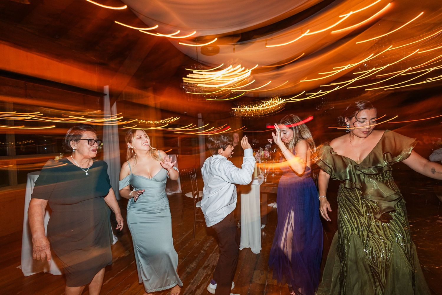 Guests dancing energetically at a wedding reception with warm golden light streaks filling the elegant venue.