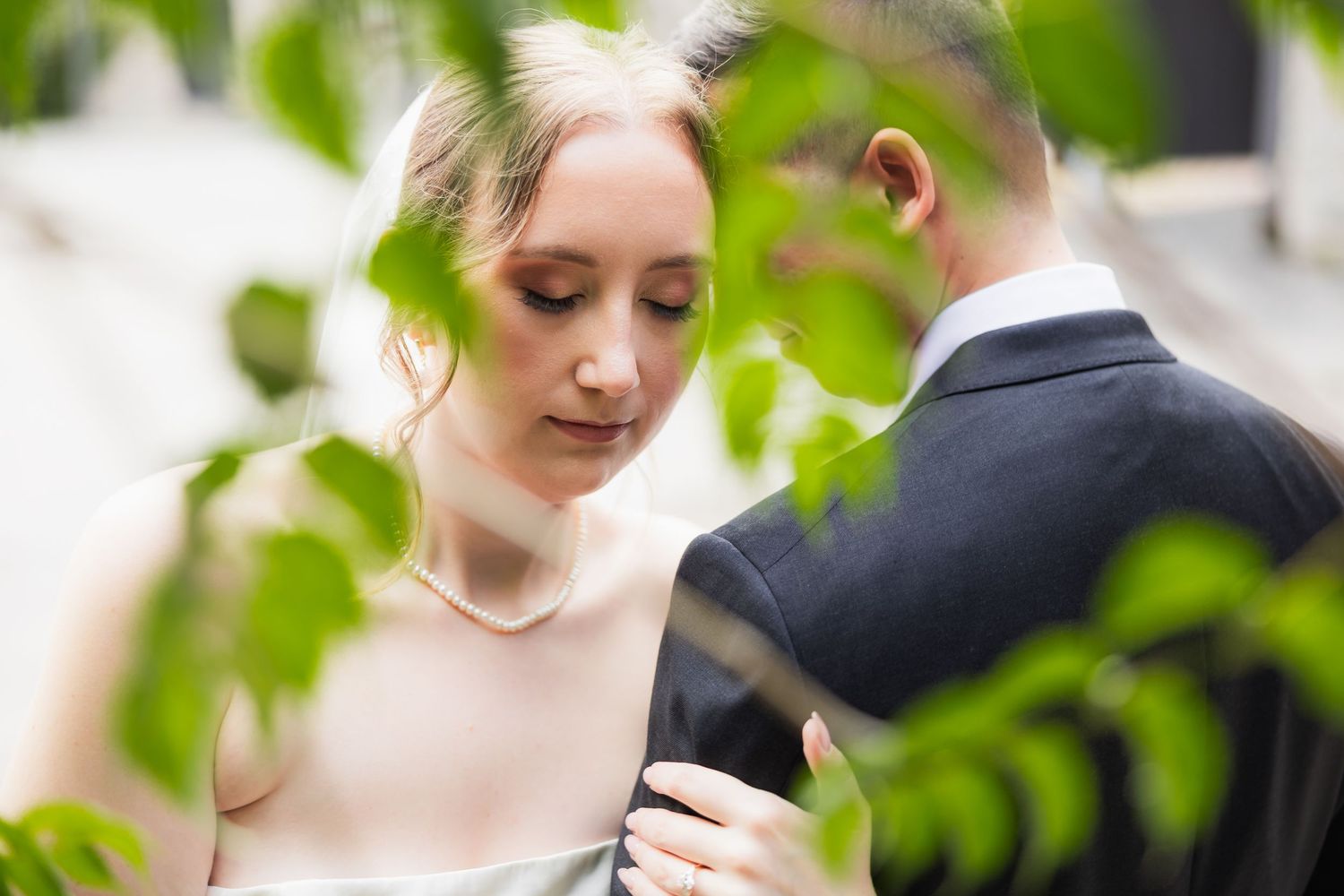 A bride and groom share an intimate moment framed by lush green leaves during their wedding day.