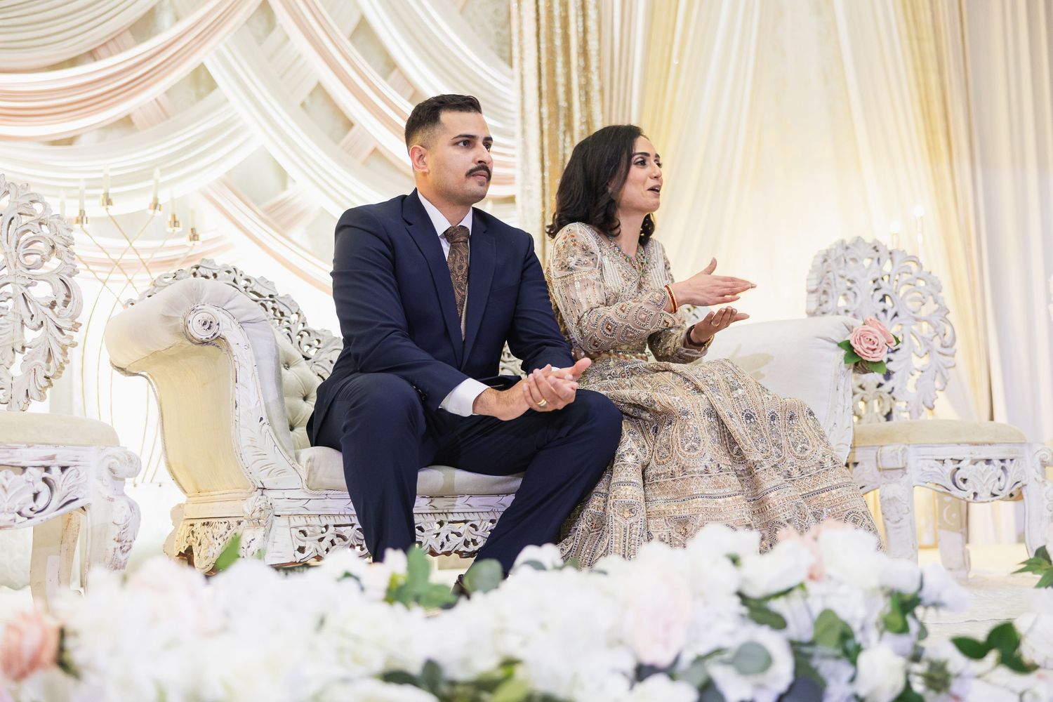 Elegant wedding reception venue with white floral arrangements and ornate decor along a head table.