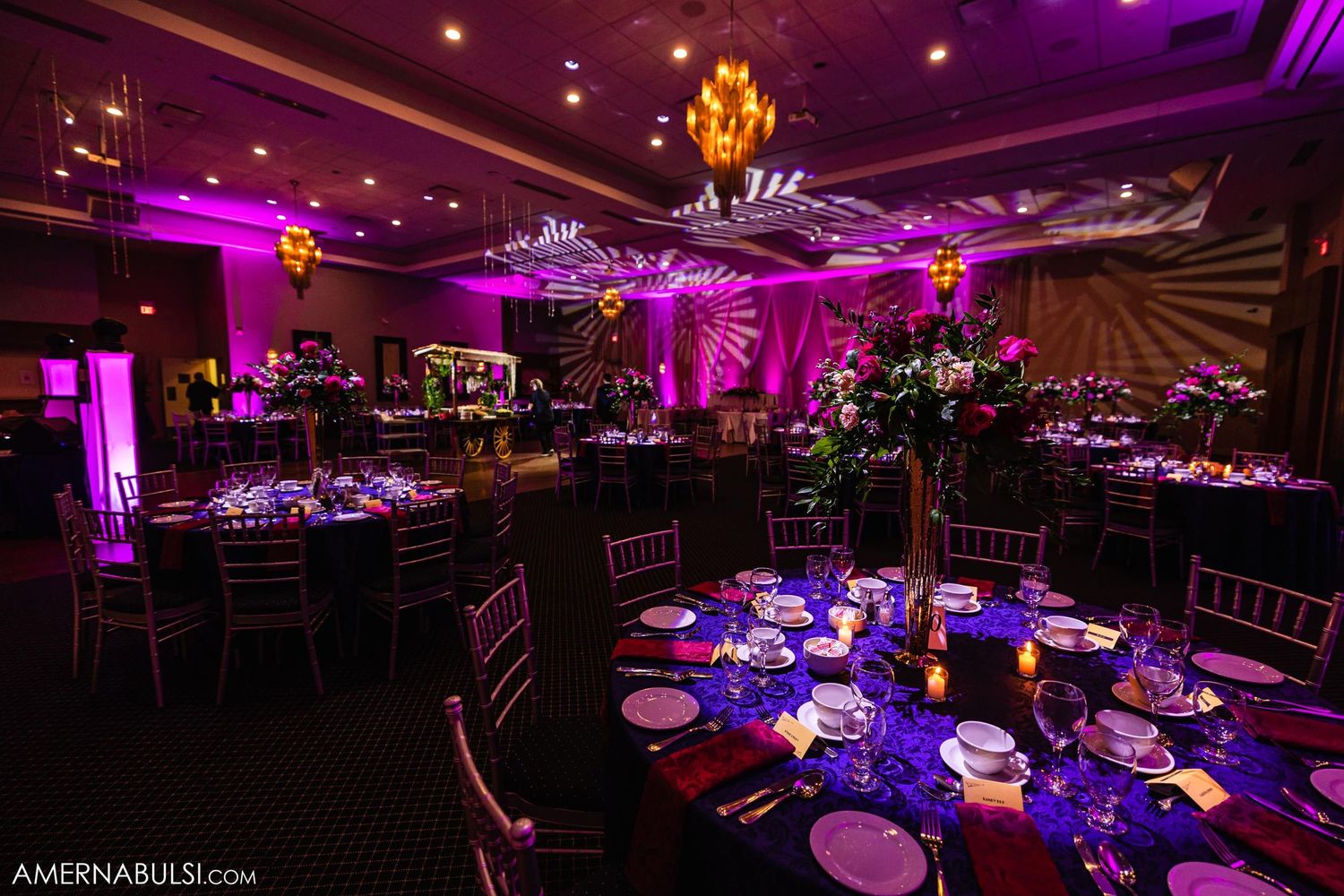 Elegant ballroom reception setup with purple lighting and formal table settings.