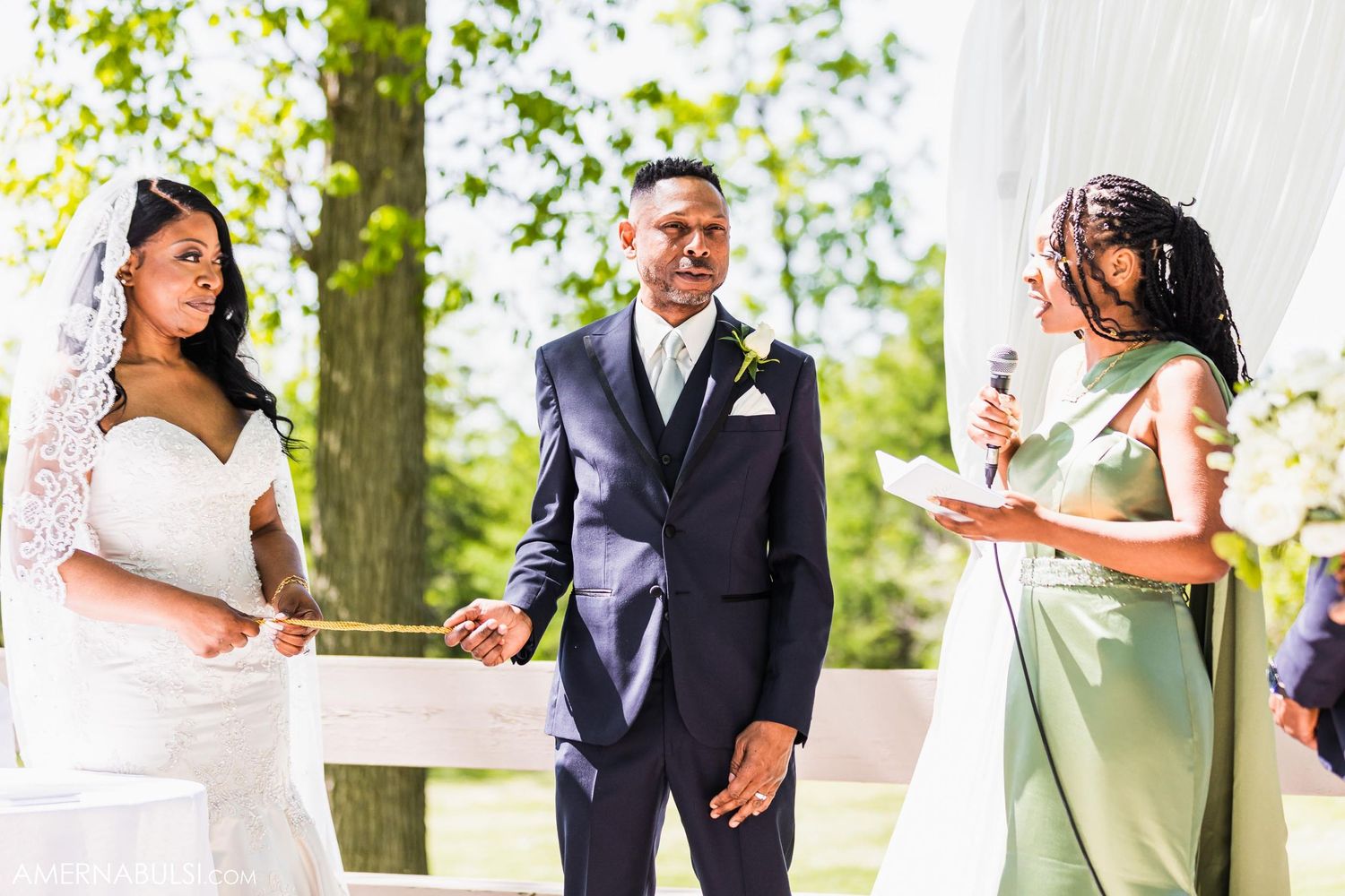 Couple exchanges vows during outdoor wedding ceremony with officiant in mint green dress.
