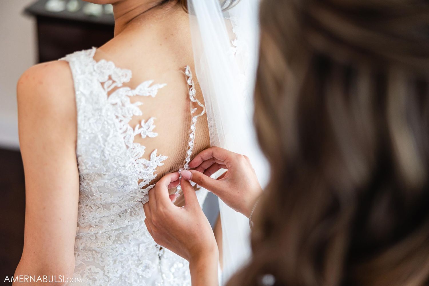 Detail shot of intricate lace buttons being fastened on back of wedding gown.