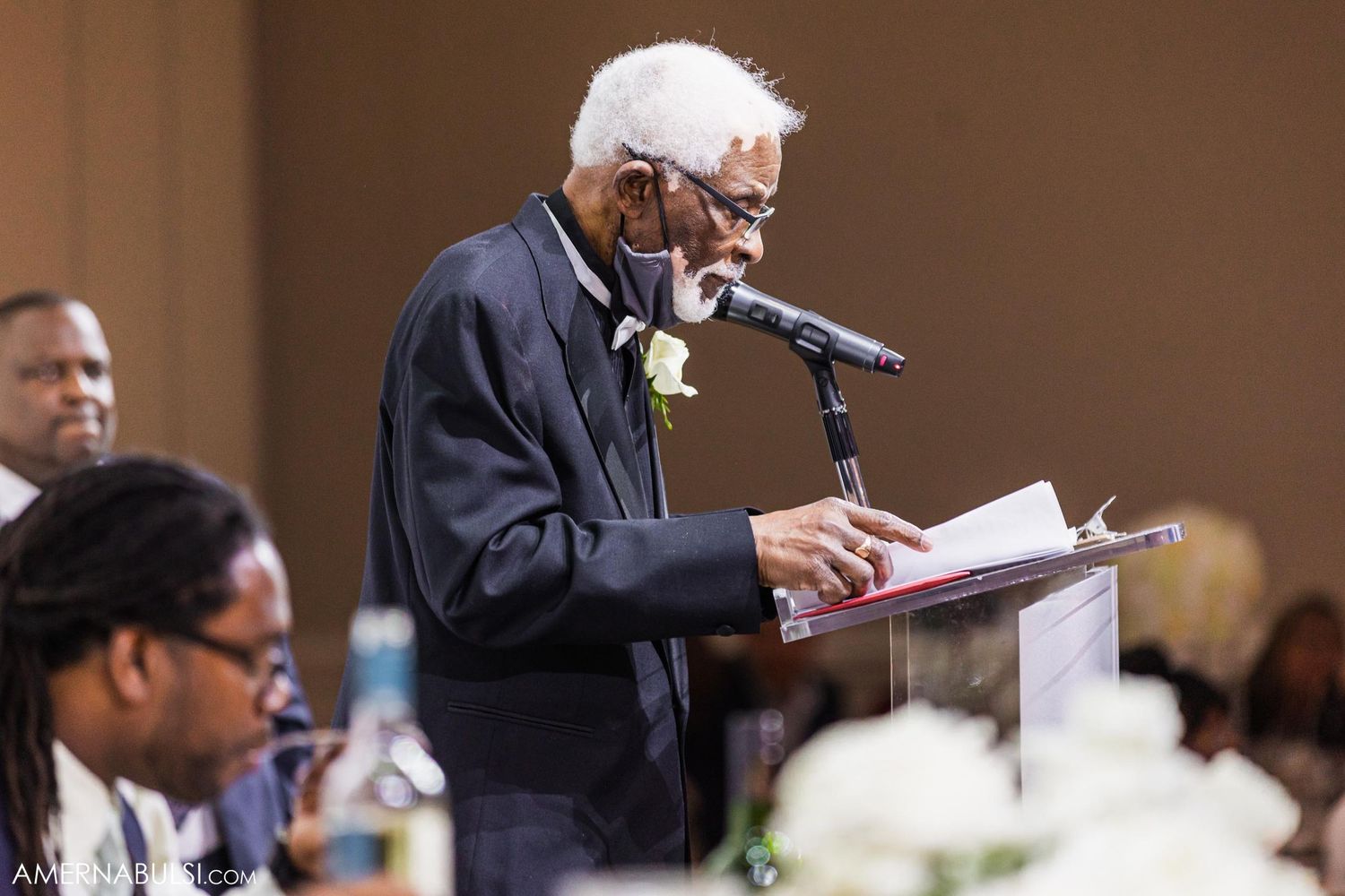 Senior speaker delivers heartfelt speech at podium during formal event.