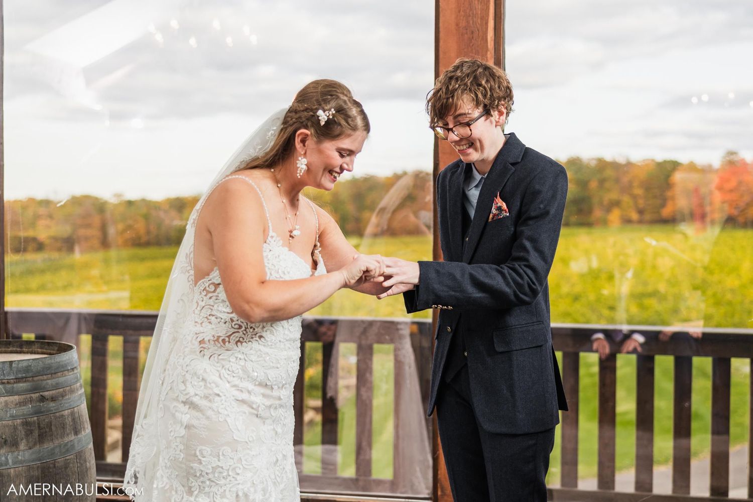 A couple shares an intimate moment during their wedding ceremony on an outdoor deck with autumn foliage in background.