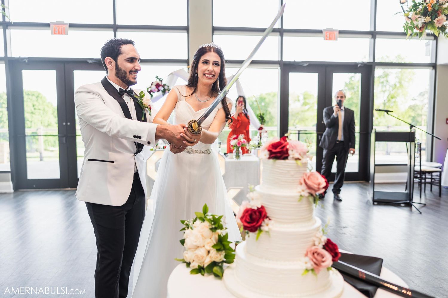 Newlyweds cutting their multi-tiered white wedding cake adorned with pink flowers.