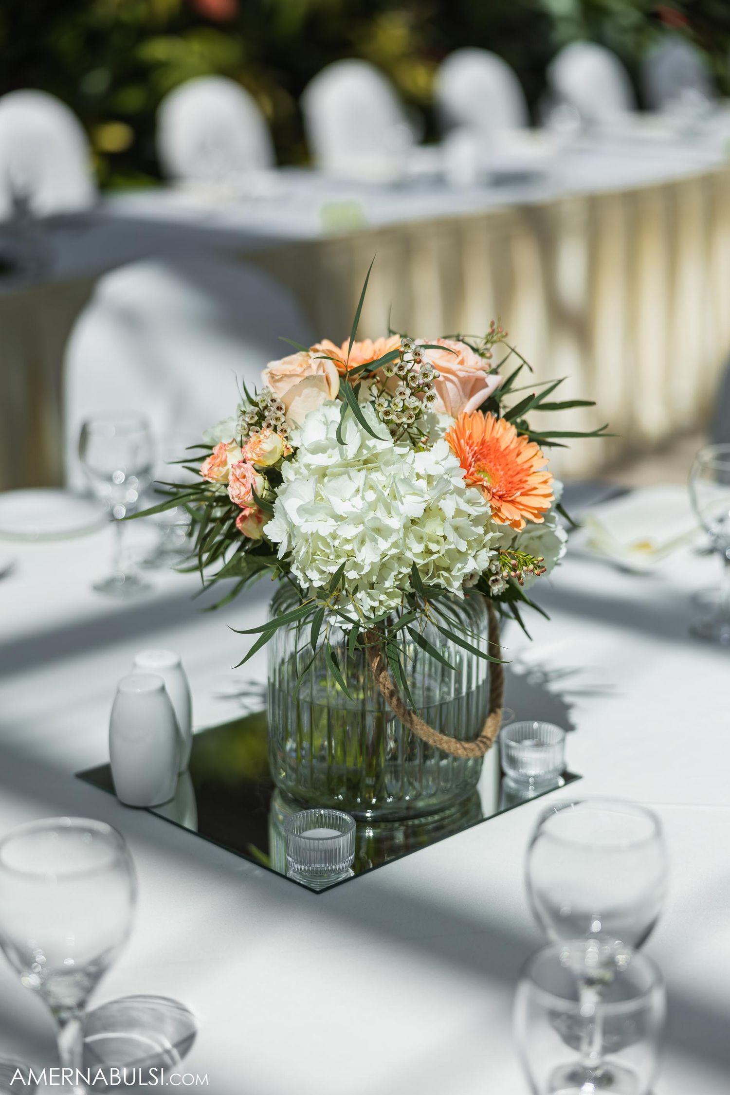 Close-up of peach and white flower centerpiece in glass vase on mirrored base.