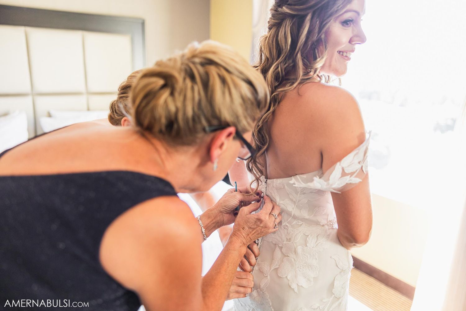 Someone helps adjust the back of a white wedding dress.