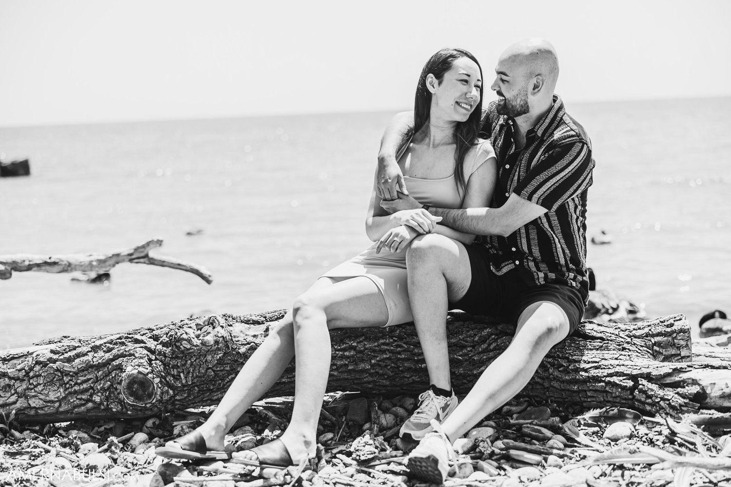 Black and white photo of a couple sharing an intimate moment on a beach log.