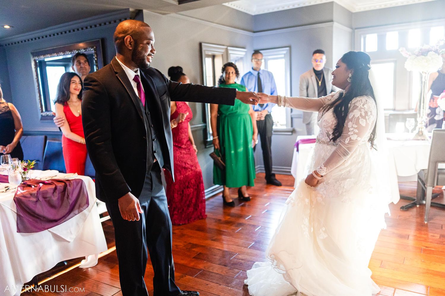 Wedding couple sharing a playful dance move in a reception hall with guests watching.
