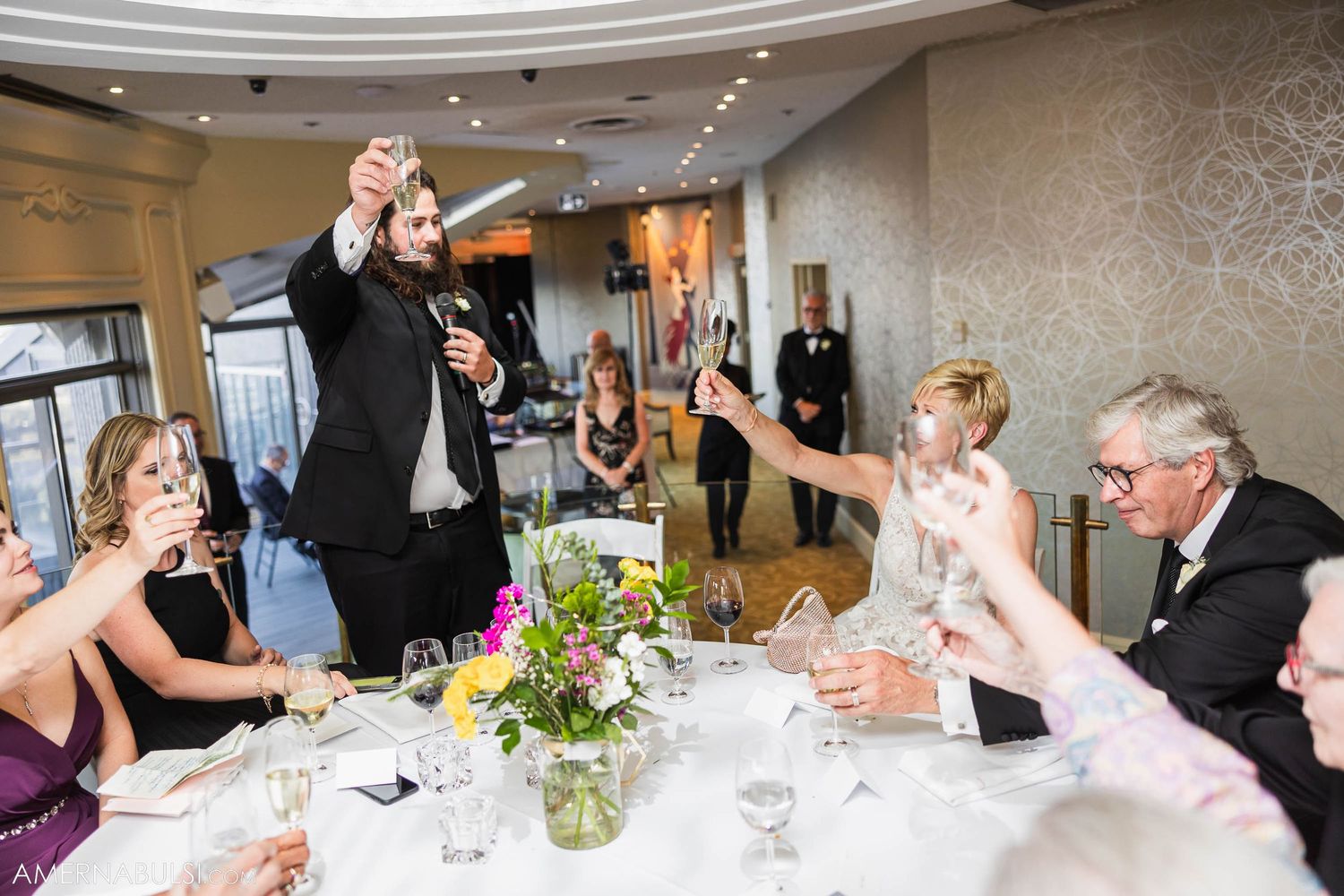 Celebratory toast among guests at elegant dinner with floral centerpieces.