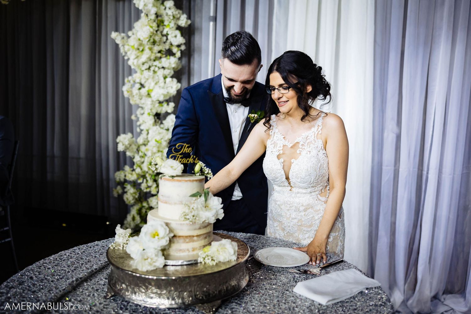 Newlyweds cutting their elegant white wedding cake together at their reception.
