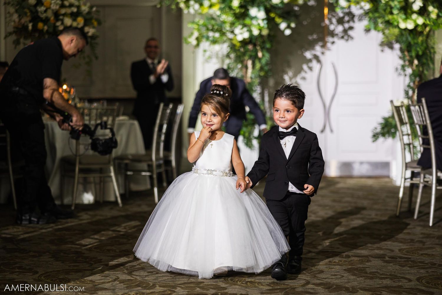 Two young children in formal attire share a sweet moment at an elegant wedding reception.