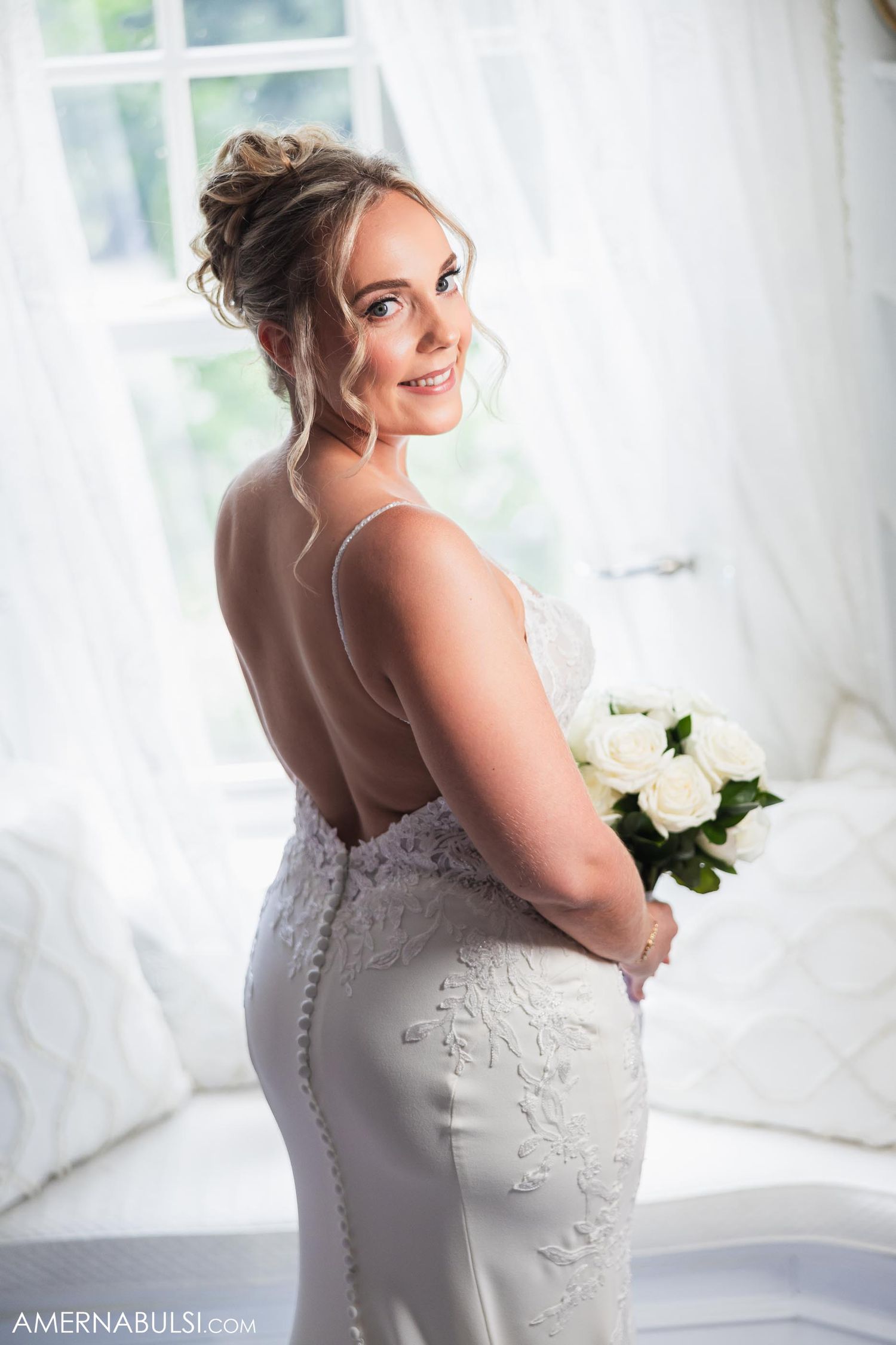 Bridal portrait in front of bright window showcasing elegant wedding gown and styling.