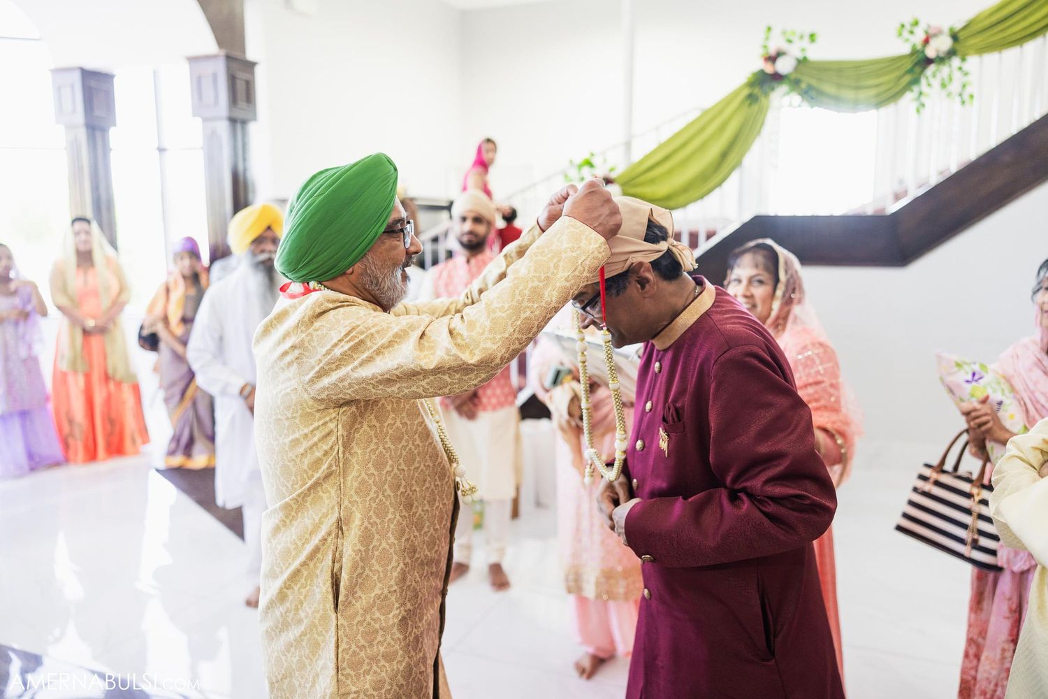 Traditional ceremonial moment with participants in festive Indian attire under decorative green draping.