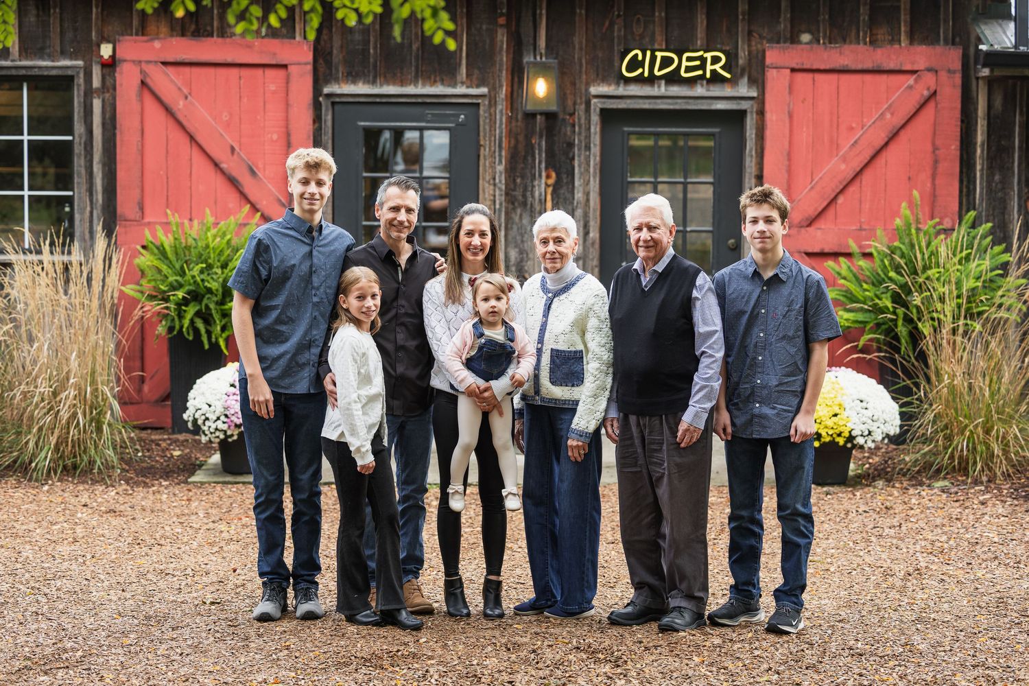 Family group poses together in front of a rustic red barn on a fall day.