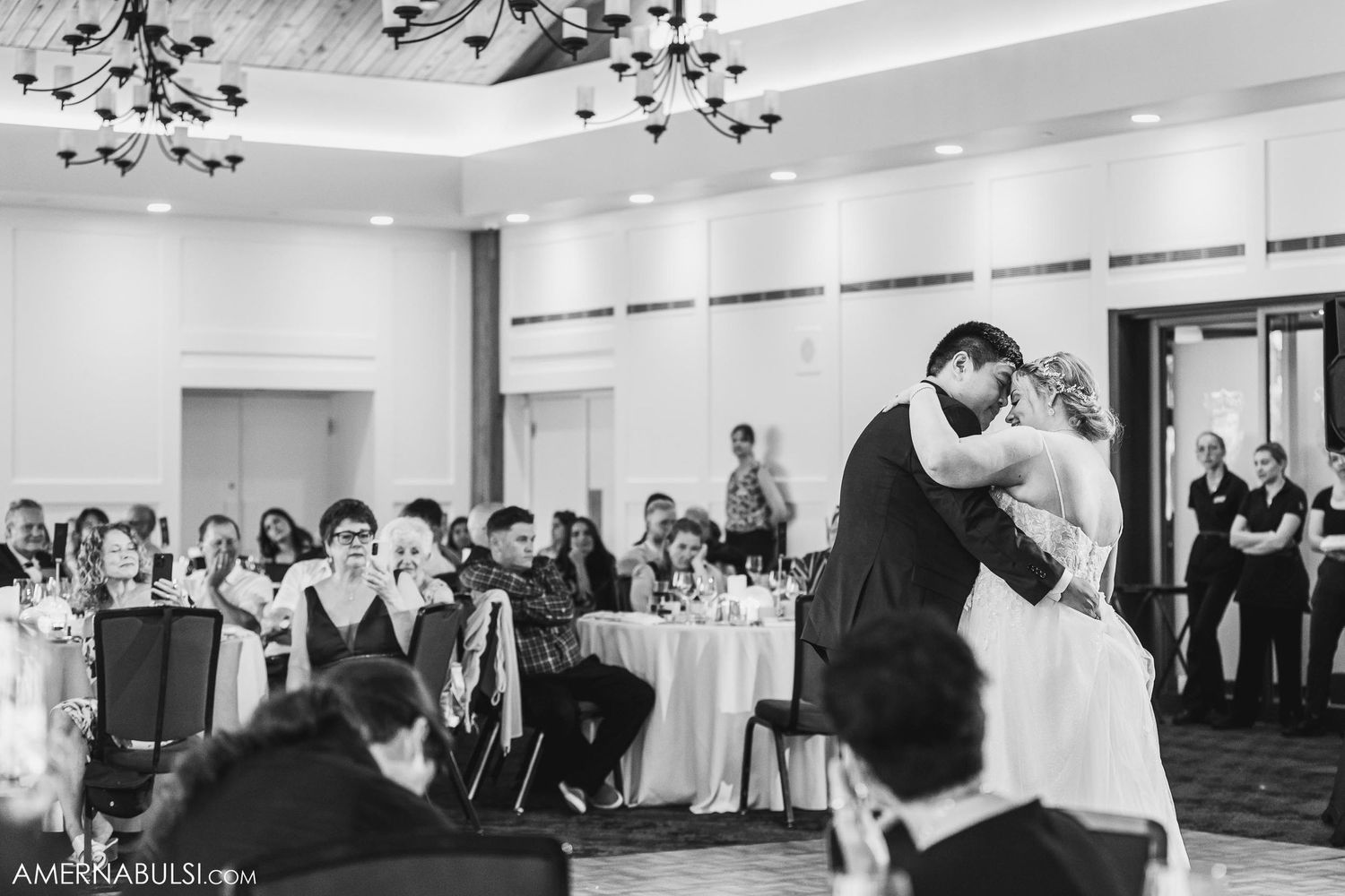 Black and white photo of couple's first dance at wedding reception with guests watching.