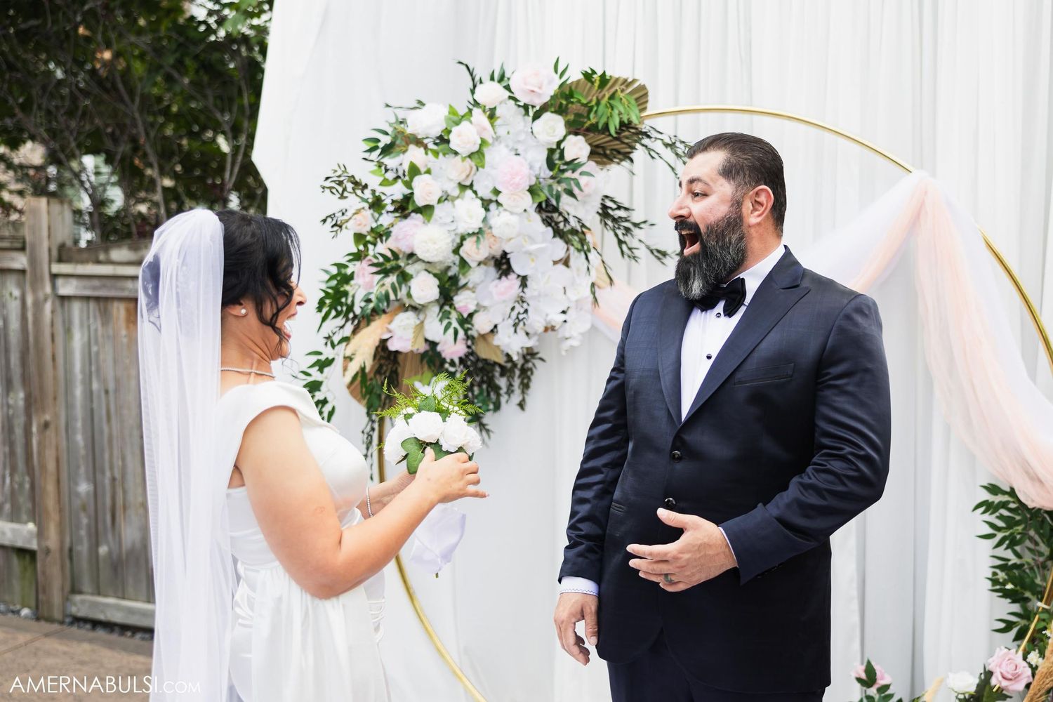 Newlyweds share emotional first look moment in front of decorative floral arch.