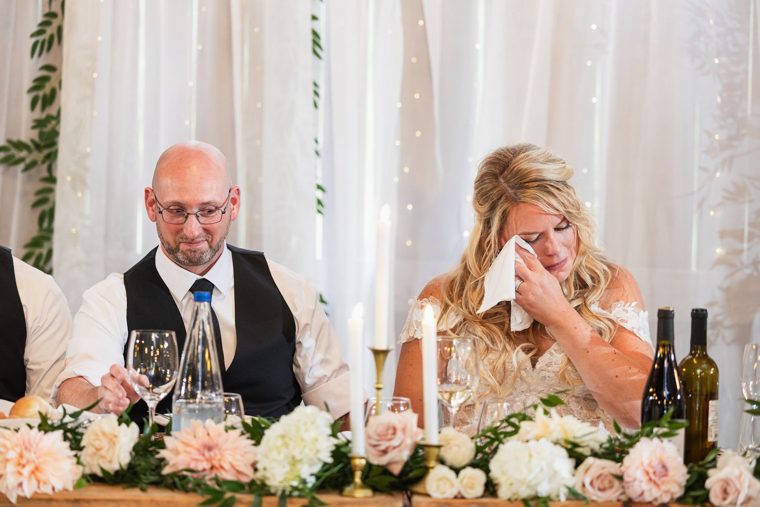 Wedding reception table decorated with pink and white flowers against white fabric backdrop.