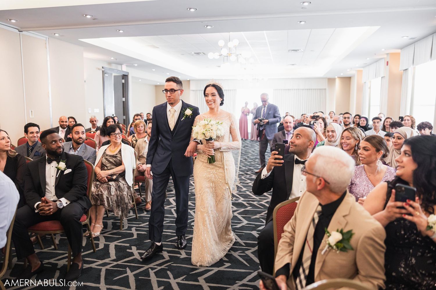 Wedding processional in a modern venue with geometric carpet and bright lighting.