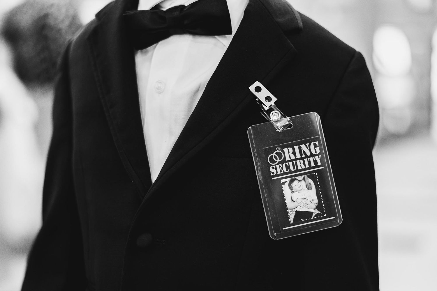 A black and white close-up of a ring bearer security badge attached to a formal suit.