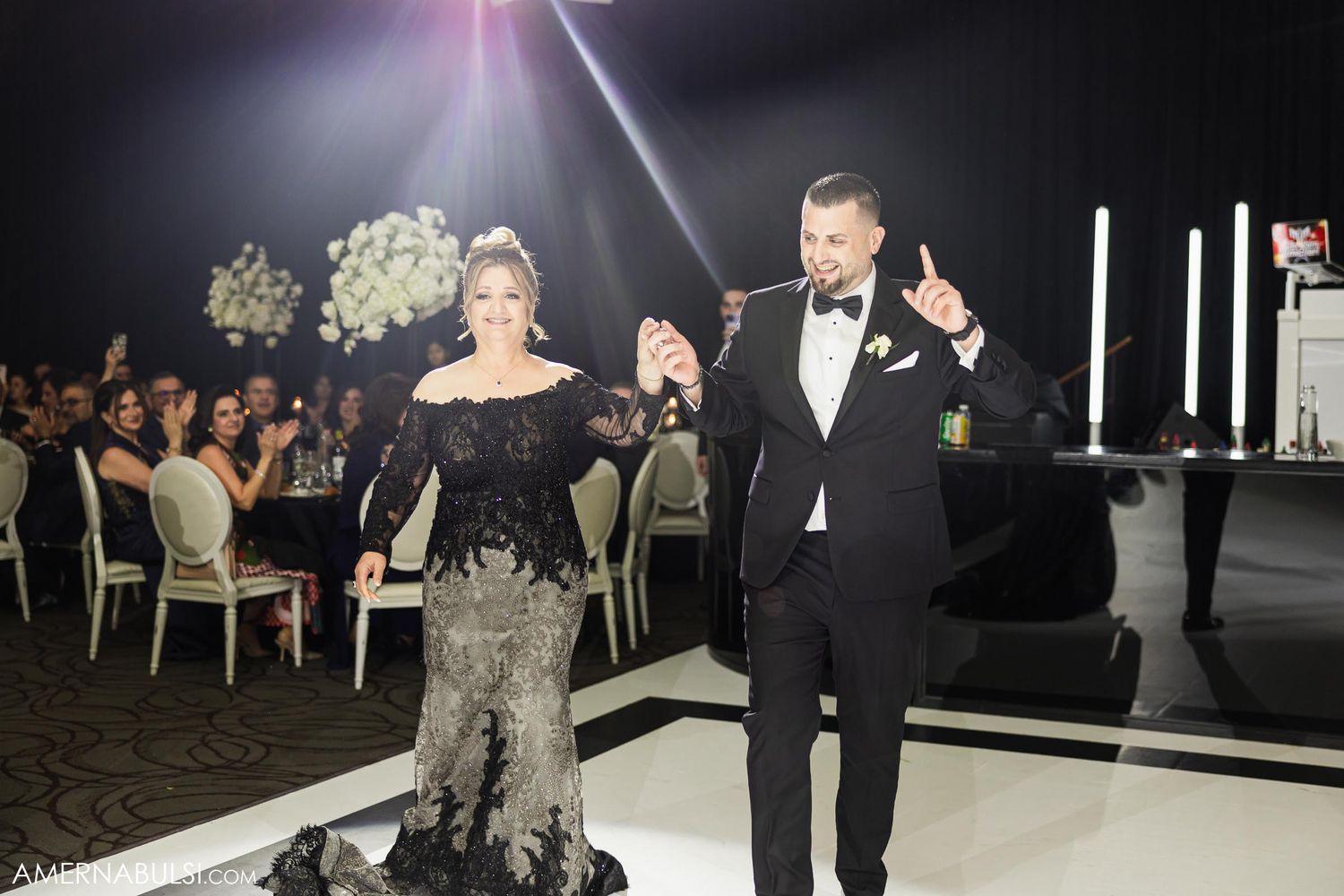 Elegant couple dancing during reception with guests and floral arrangements in the background.