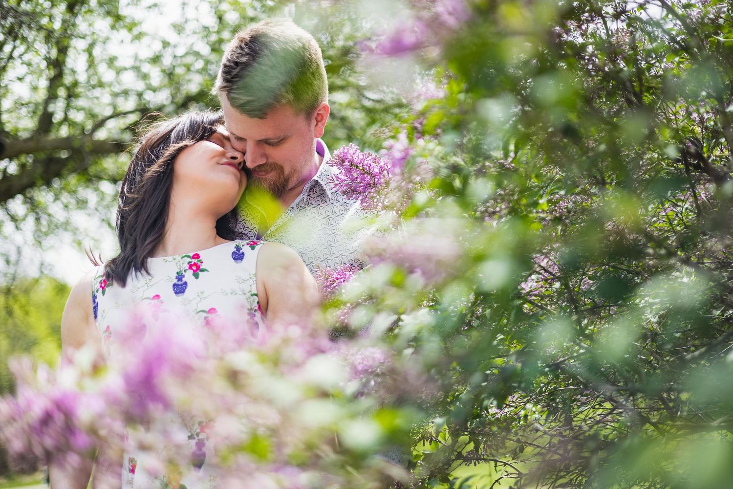 Intimate couple shares a tender moment among blooming purple flowers in a spring garden setting.