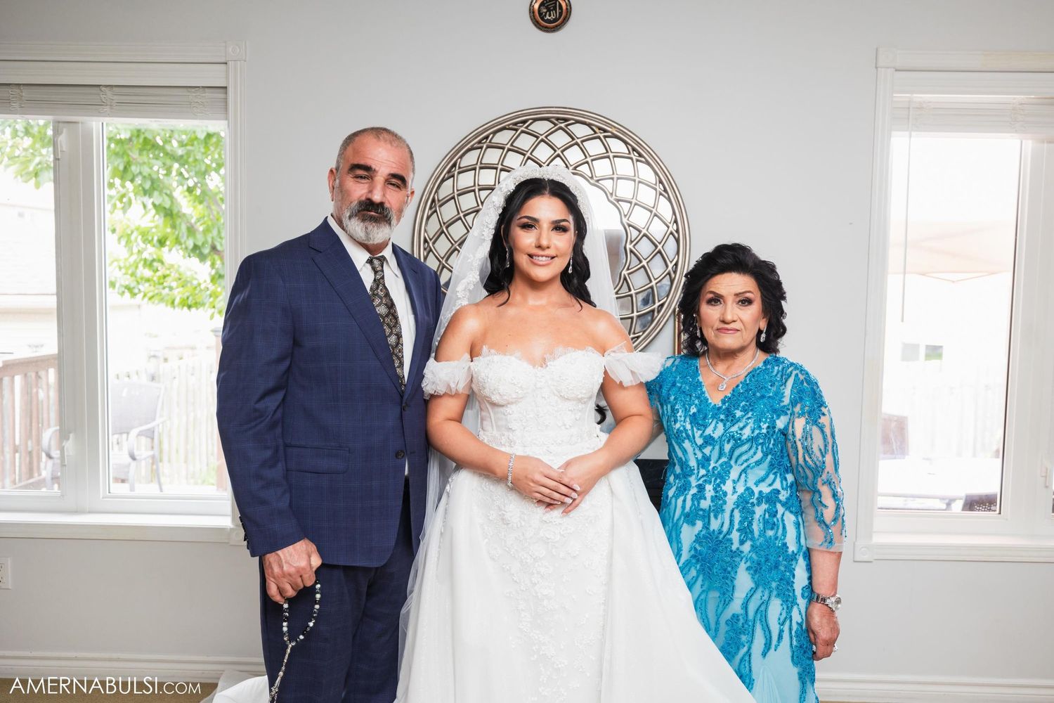 Formal family portrait in bright interior room with decorative mirror and windows.