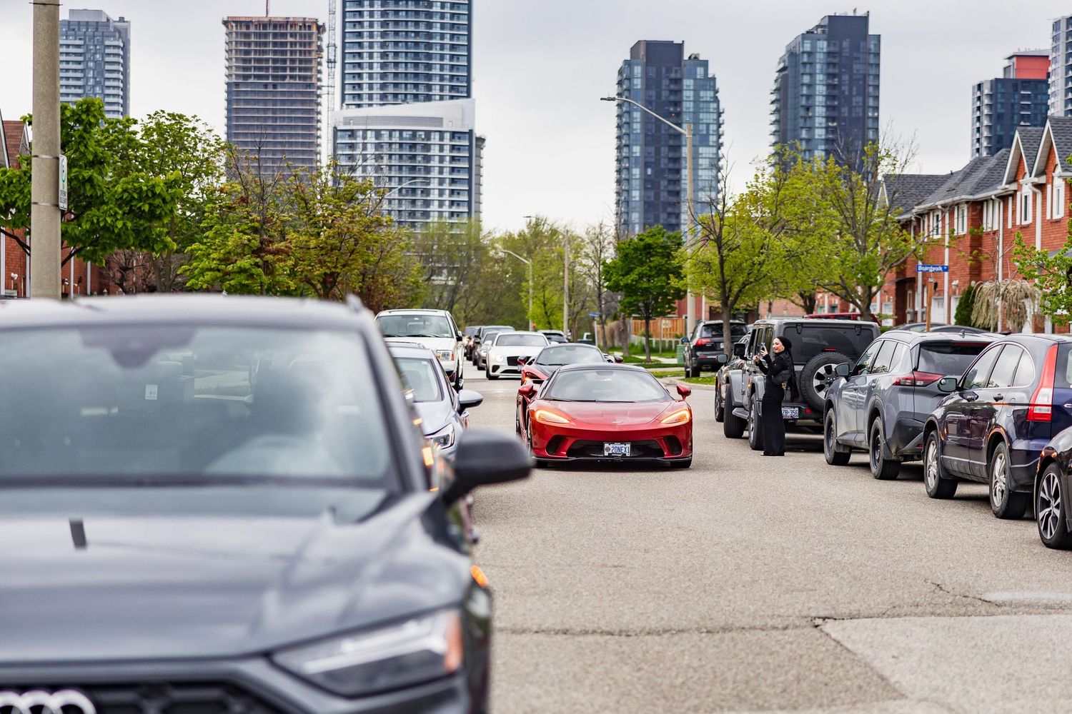 A red sports car stands out among parked vehicles on a city street with high-rise buildings.