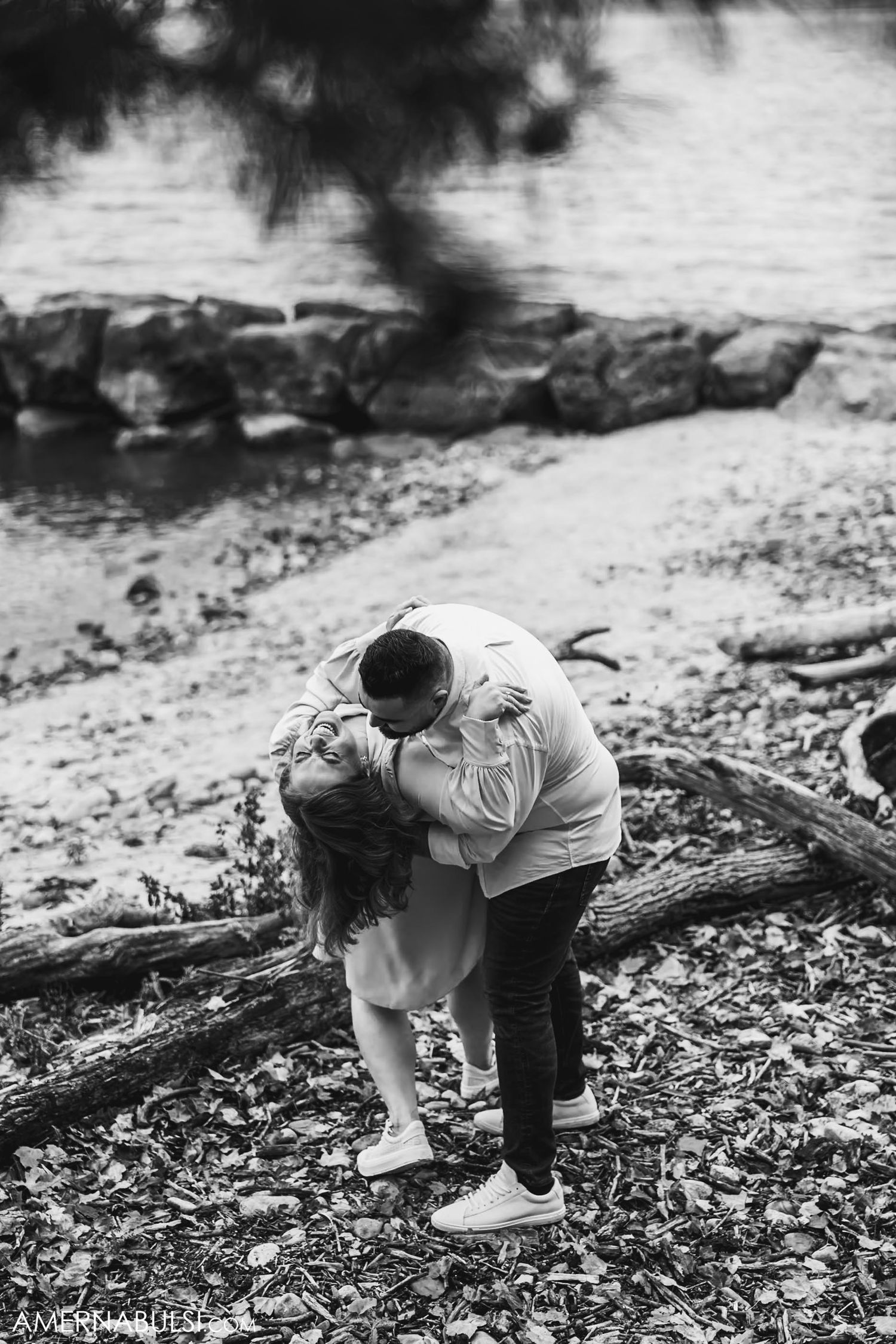 A tender embrace captured in black and white near a rocky waterfront.