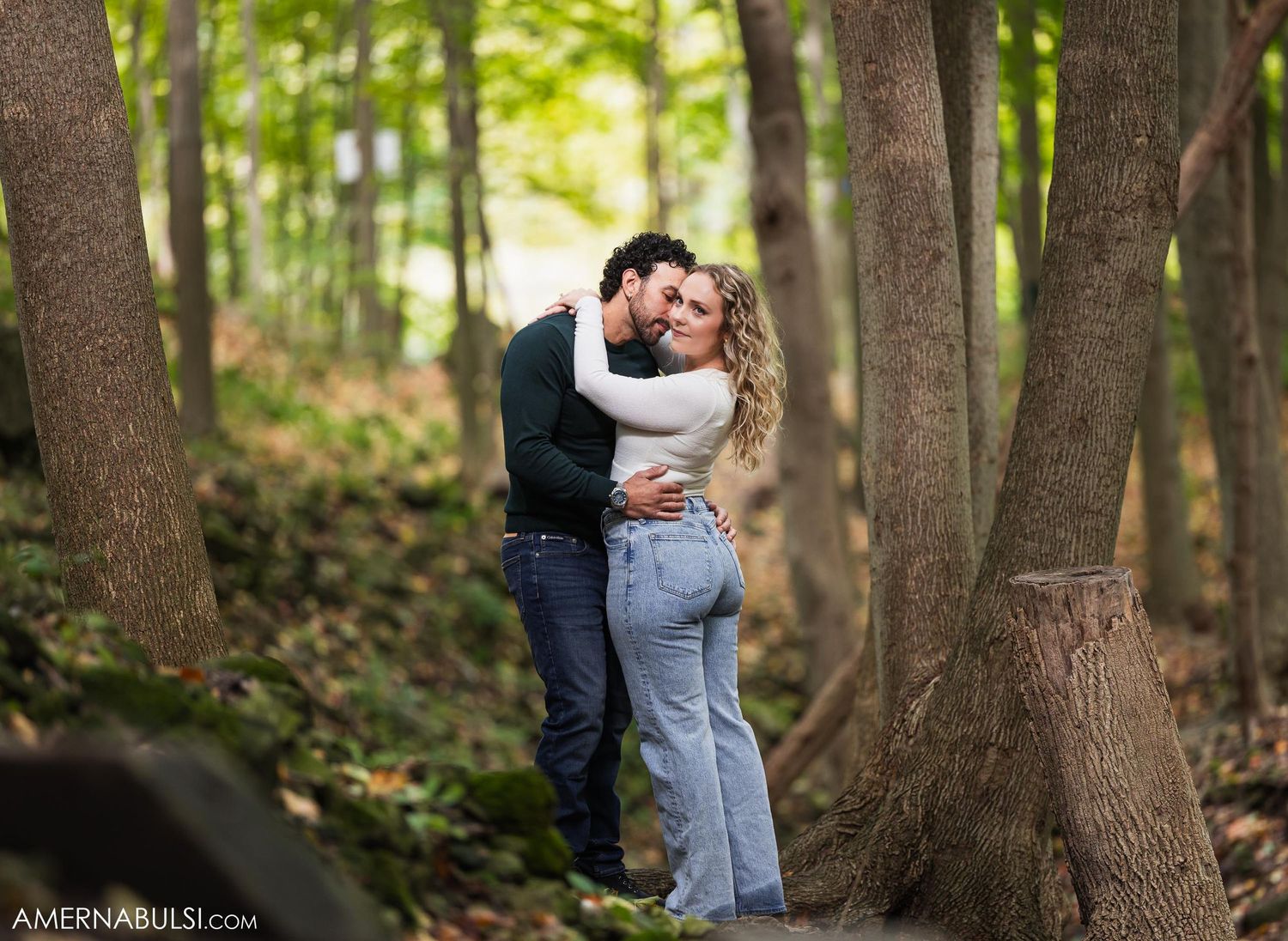 An intimate moment shared between a couple among tree trunks in a forest setting.