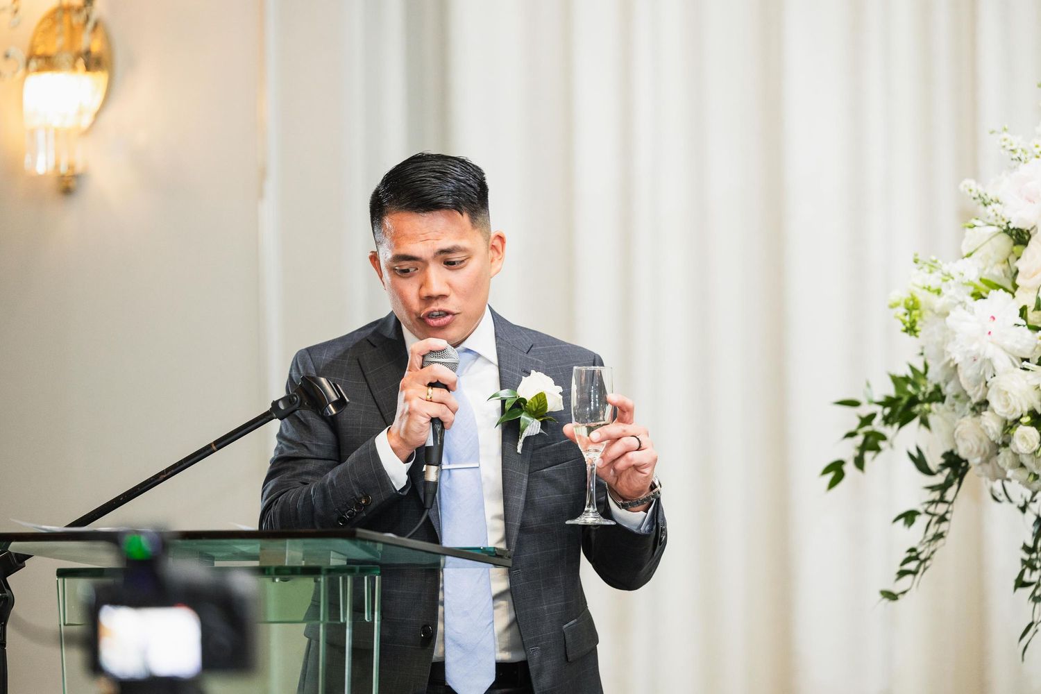 Guest delivers speech at wedding reception while holding microphone and drink.