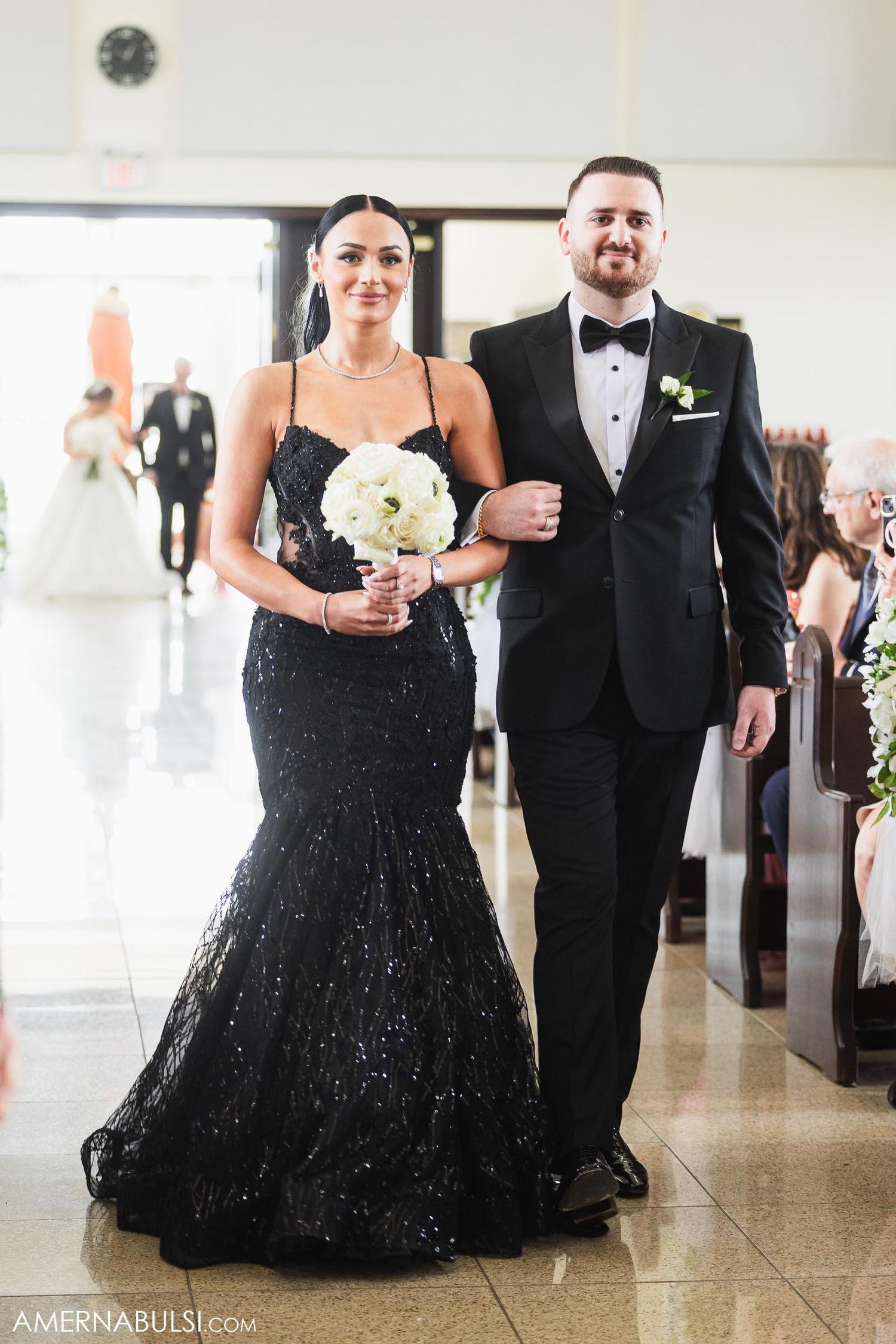 A couple in formal attire at a wedding, with the woman wearing a black sequined mermaid gown.