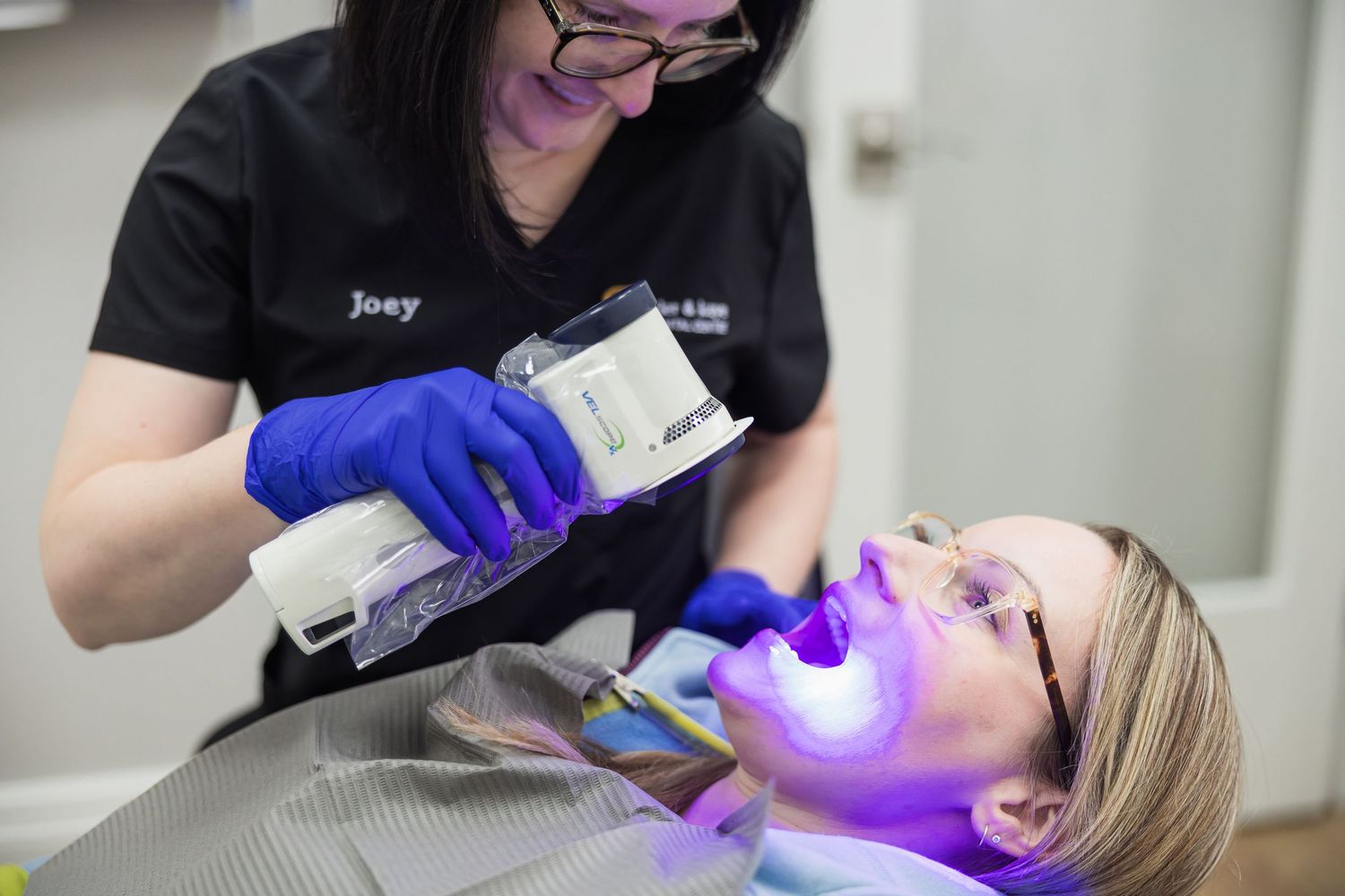 Dental hygienist Joey uses UV light teeth whitening device on a patient wearing protective glasses in a dental office.
