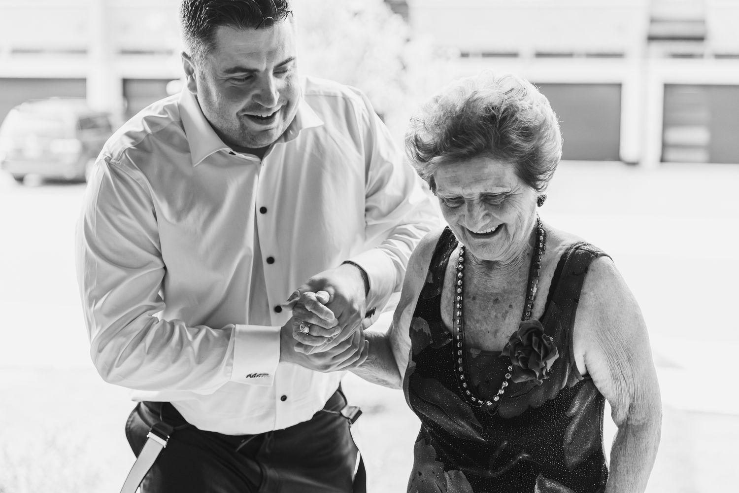 Black and white photo of groom helping elderly woman walk outdoors.