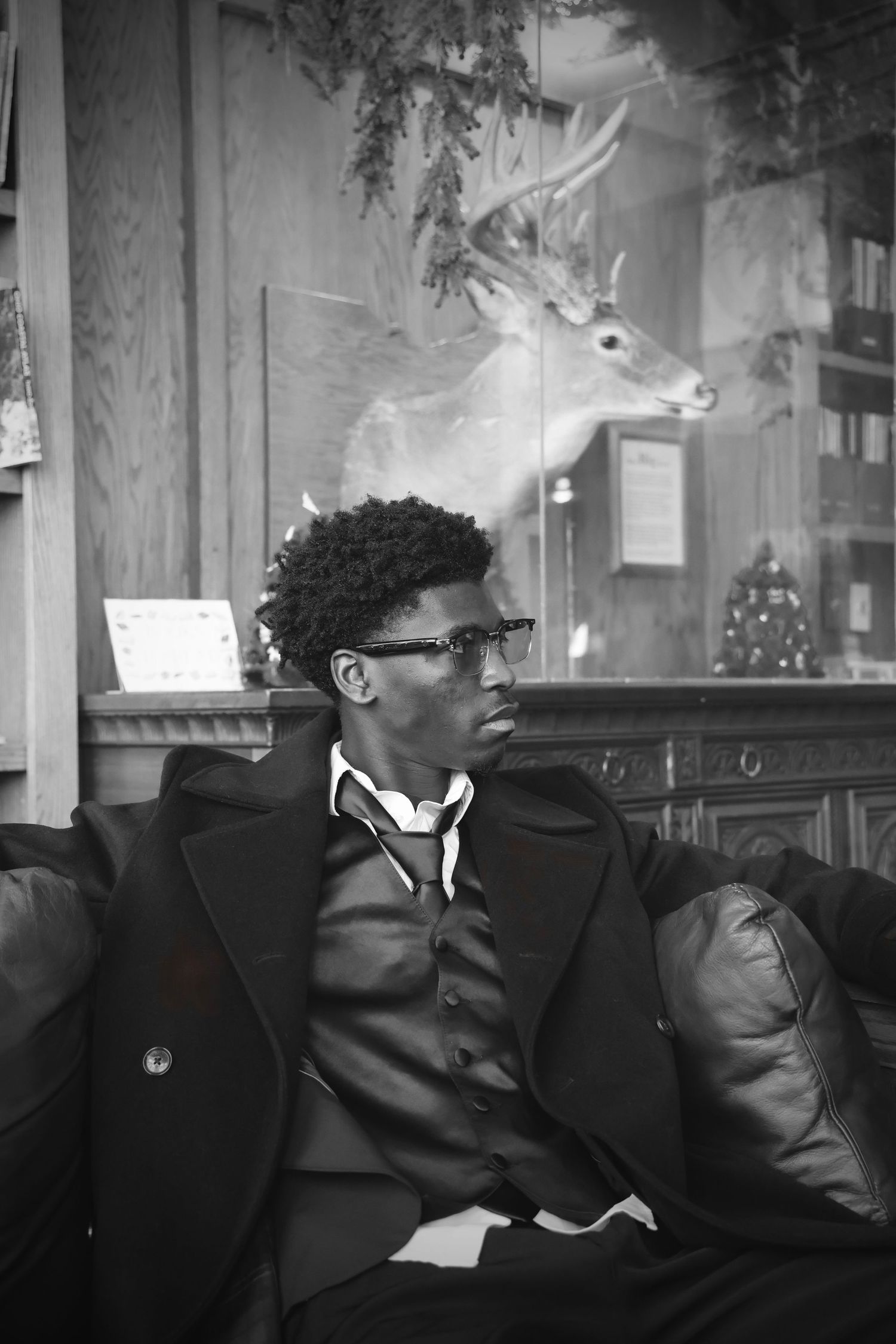 Stylish young Black man in a suit sitting on a leather sofa in a classic interior with a deer mount.