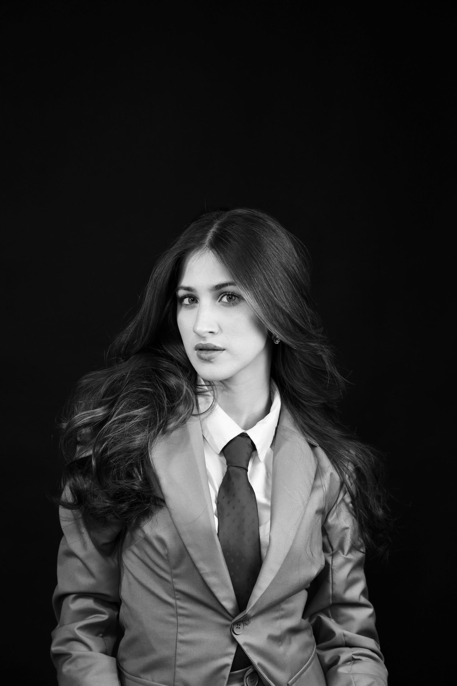 Stylish woman in blazer and tie with flowing hair in black and white photo.