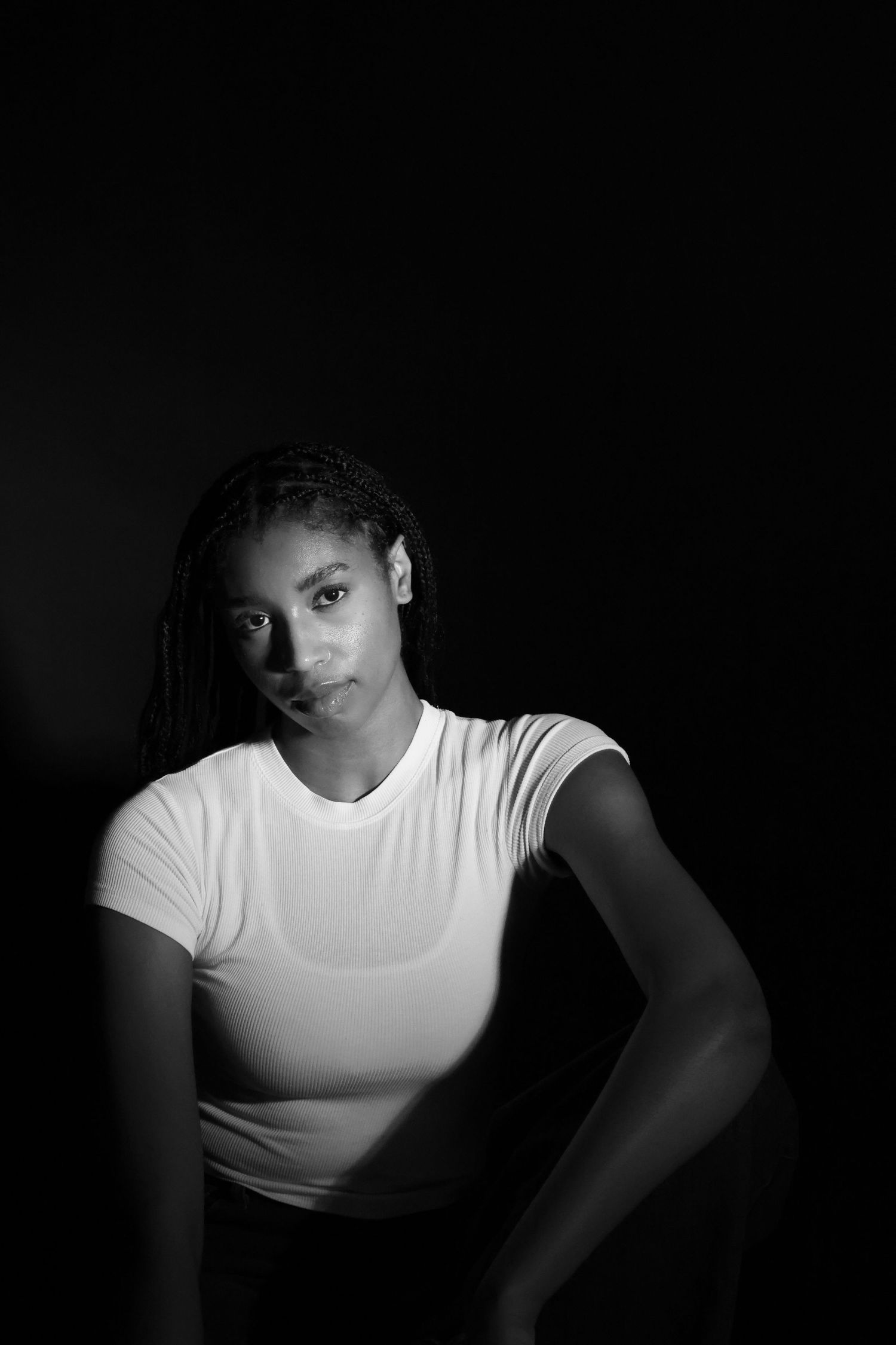 Dramatic black and white low-key portrait of a young woman in white t-shirt against dark background.