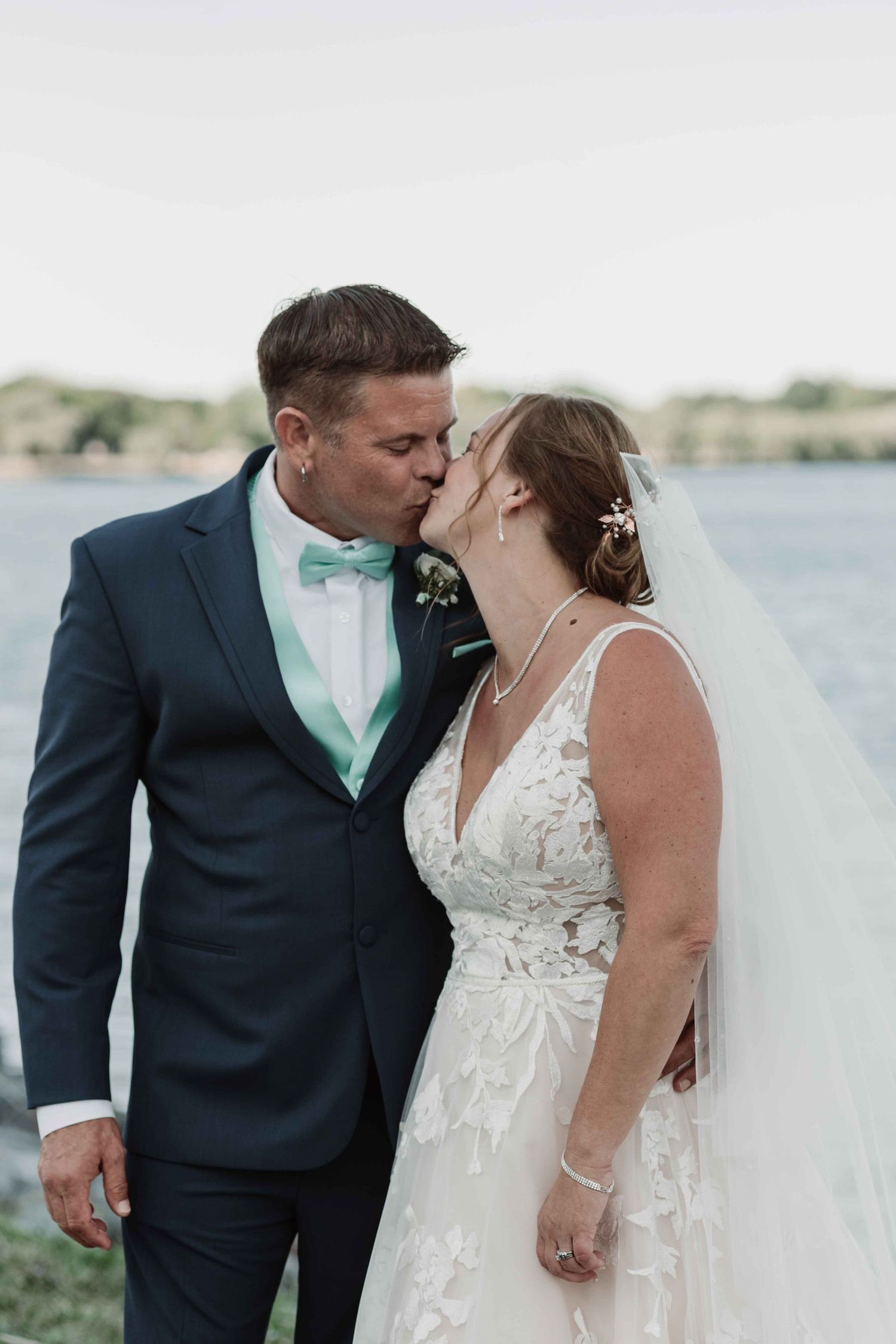Intimate waterfront wedding portraits with bride in lace dress and groom in navy suit.