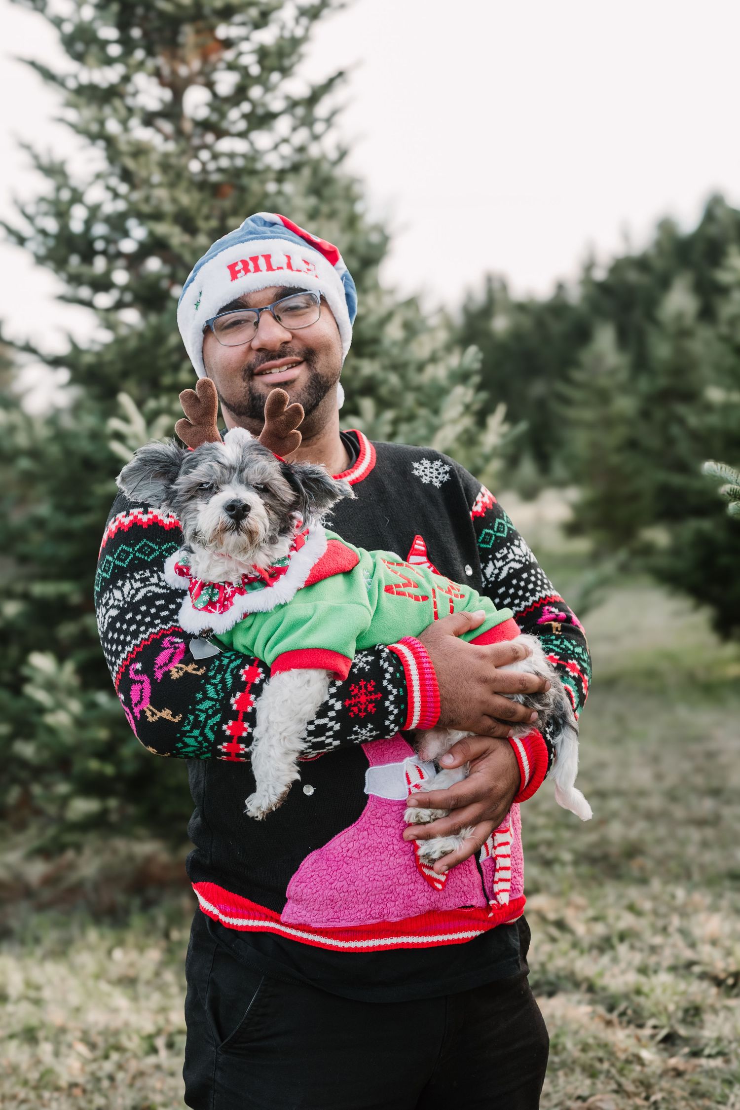 Small white dog wearing Christmas sweater posing with owner in holiday photo.