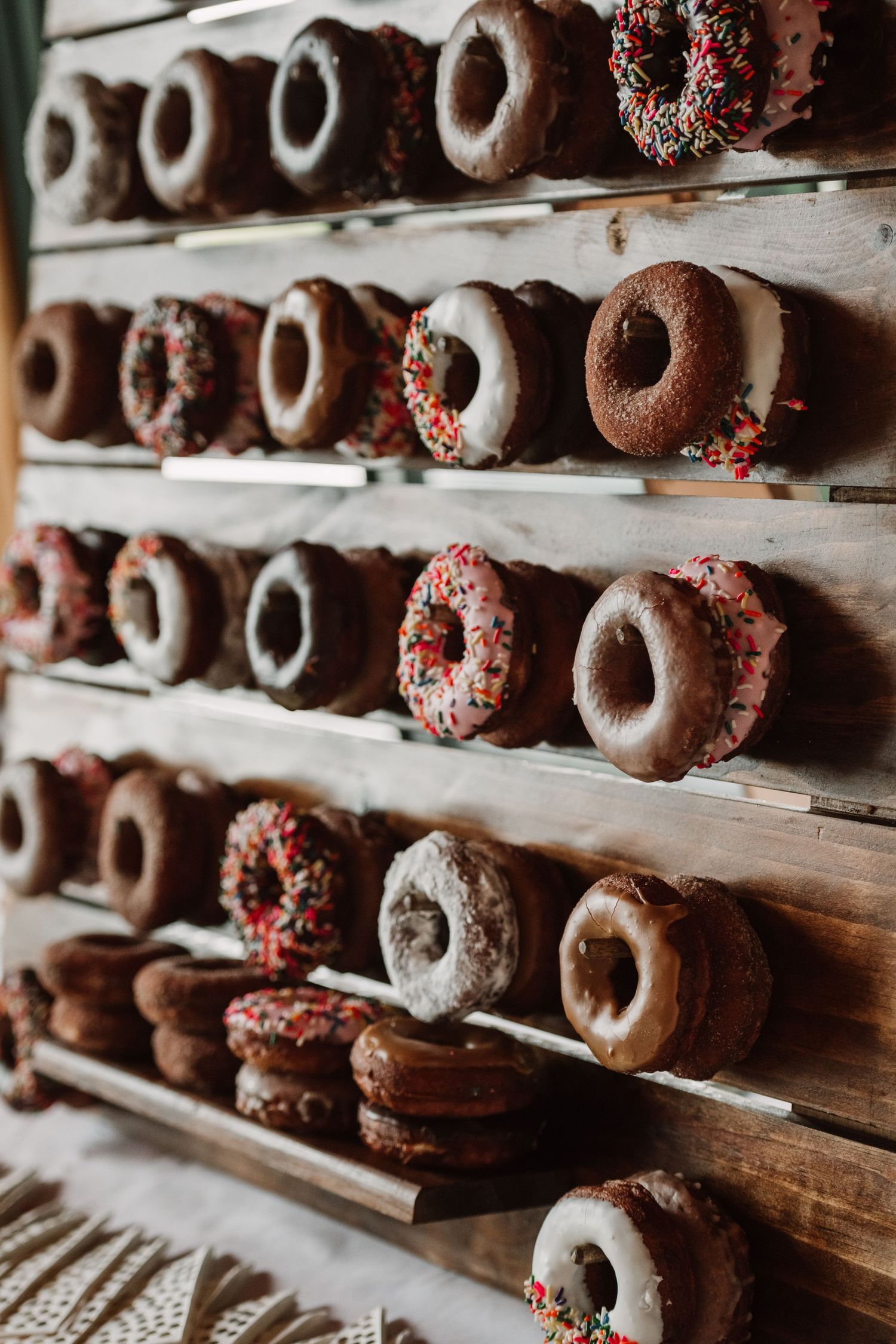 Wooden display wall filled with assorted chocolate and pink frosted donuts with colorful sprinkles at a bakery or event.