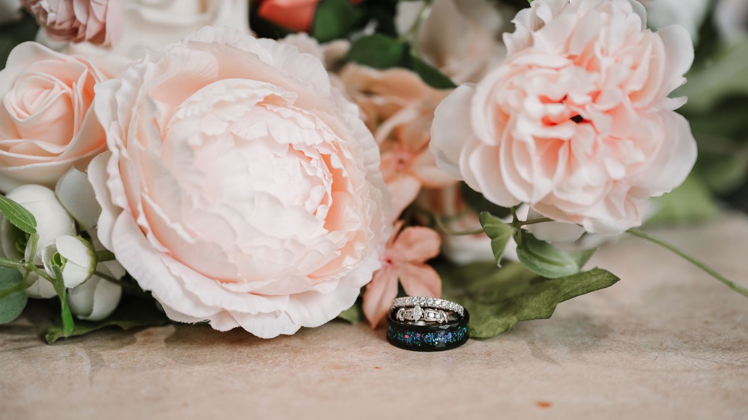 Delicate pink garden roses frame an elegant wedding ring on a textured surface.