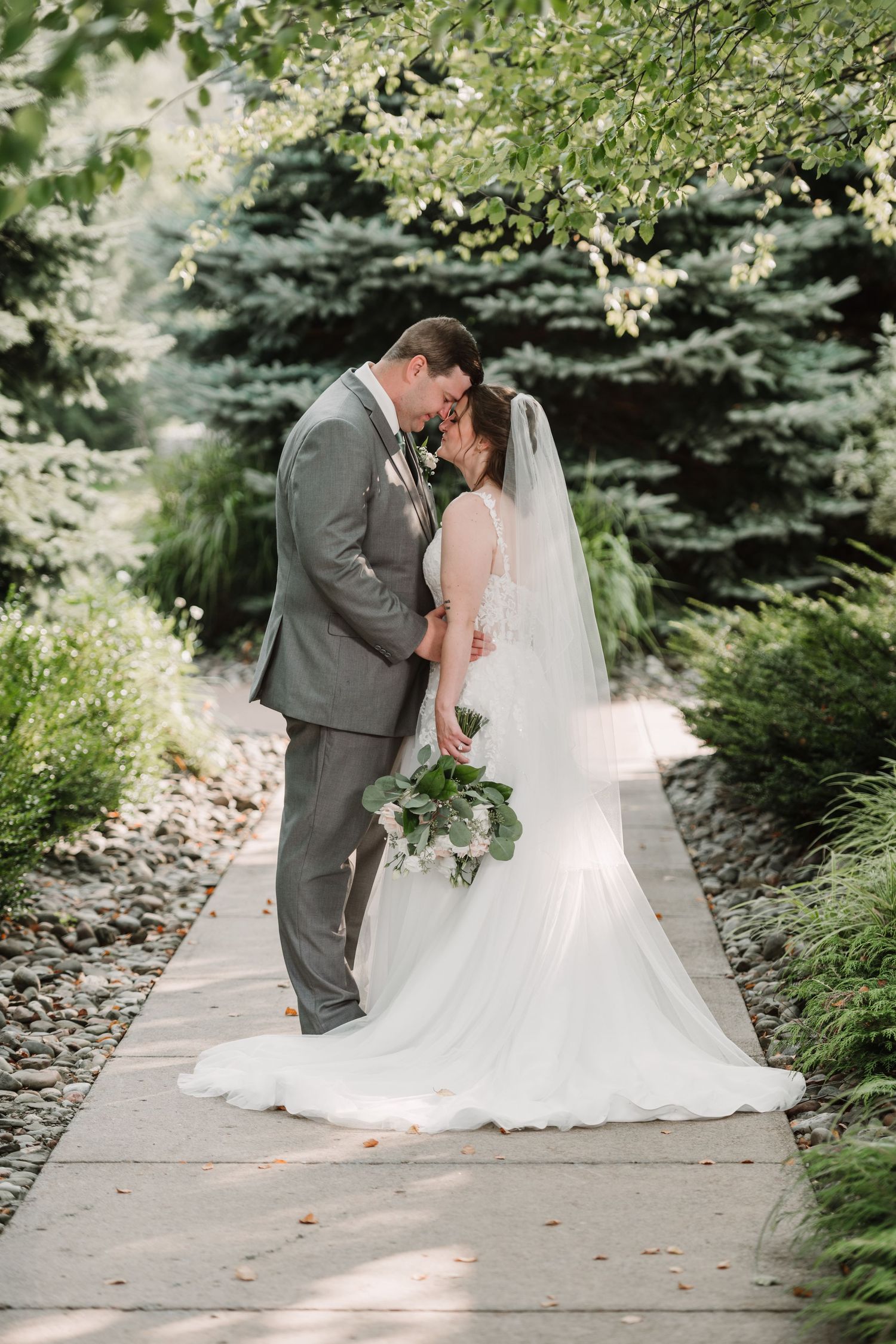 Wedding couple sharing intimate moments on a garden pathway lined with evergreens.
