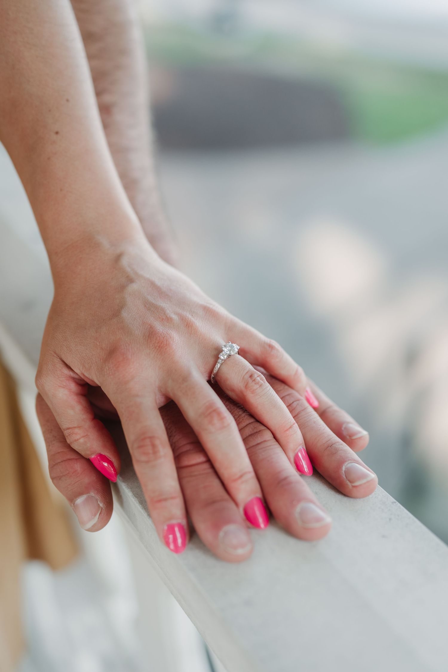 Close-up of hands with bright pink nail polish and an engagement ring.