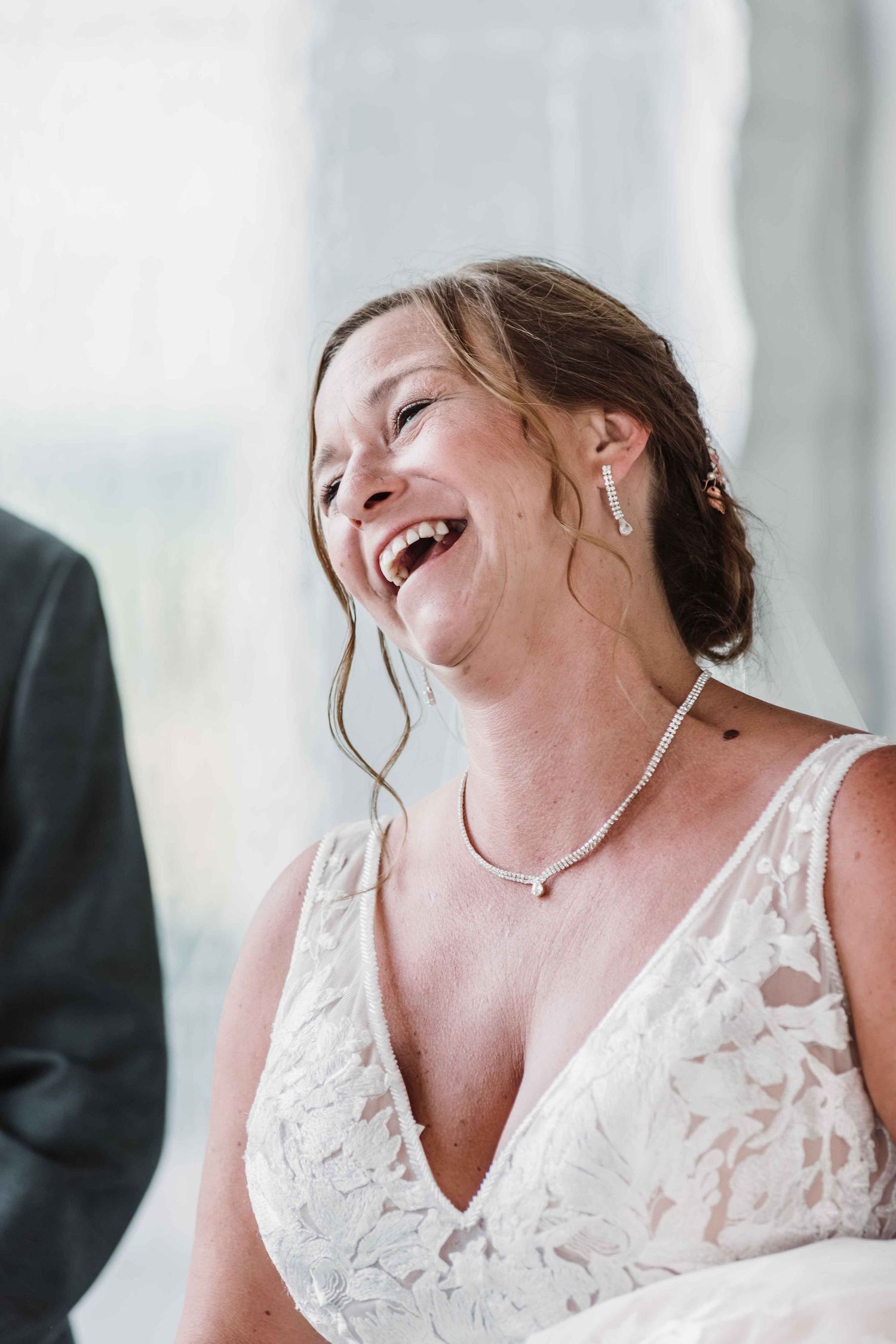 Bride in lace dress laughs joyfully during wedding celebration.