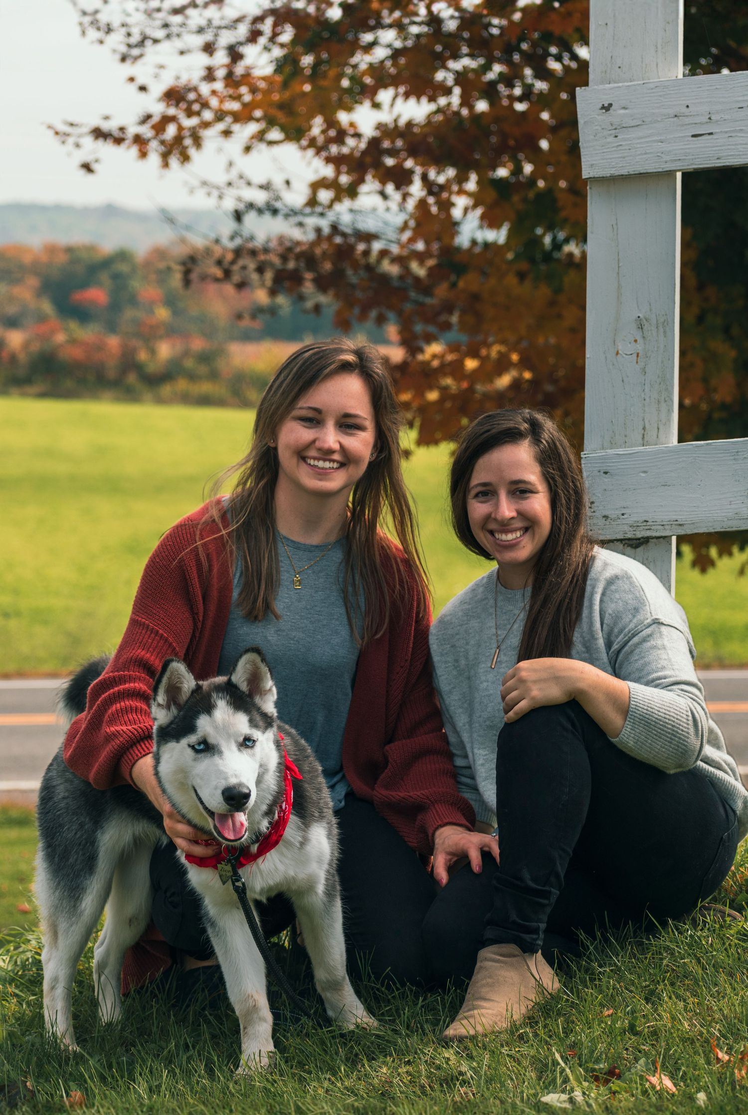 Family portrait with husky dog by white fence during fall season.