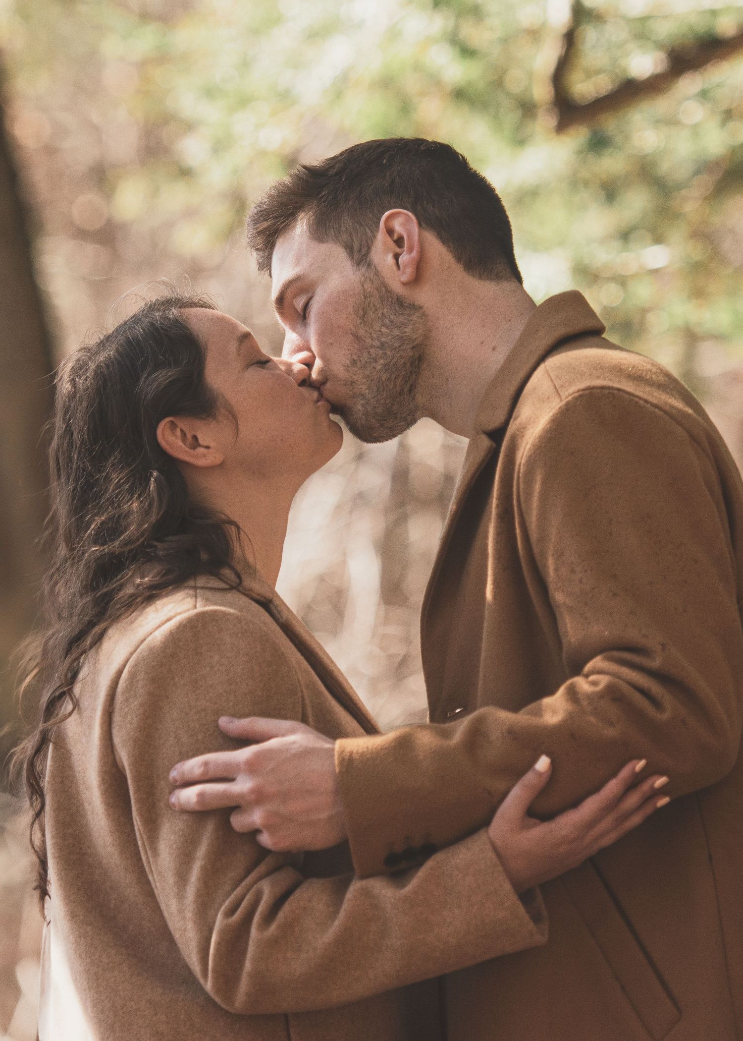 A couple in brown coats shares intimate moments in a series of romantic poses.
